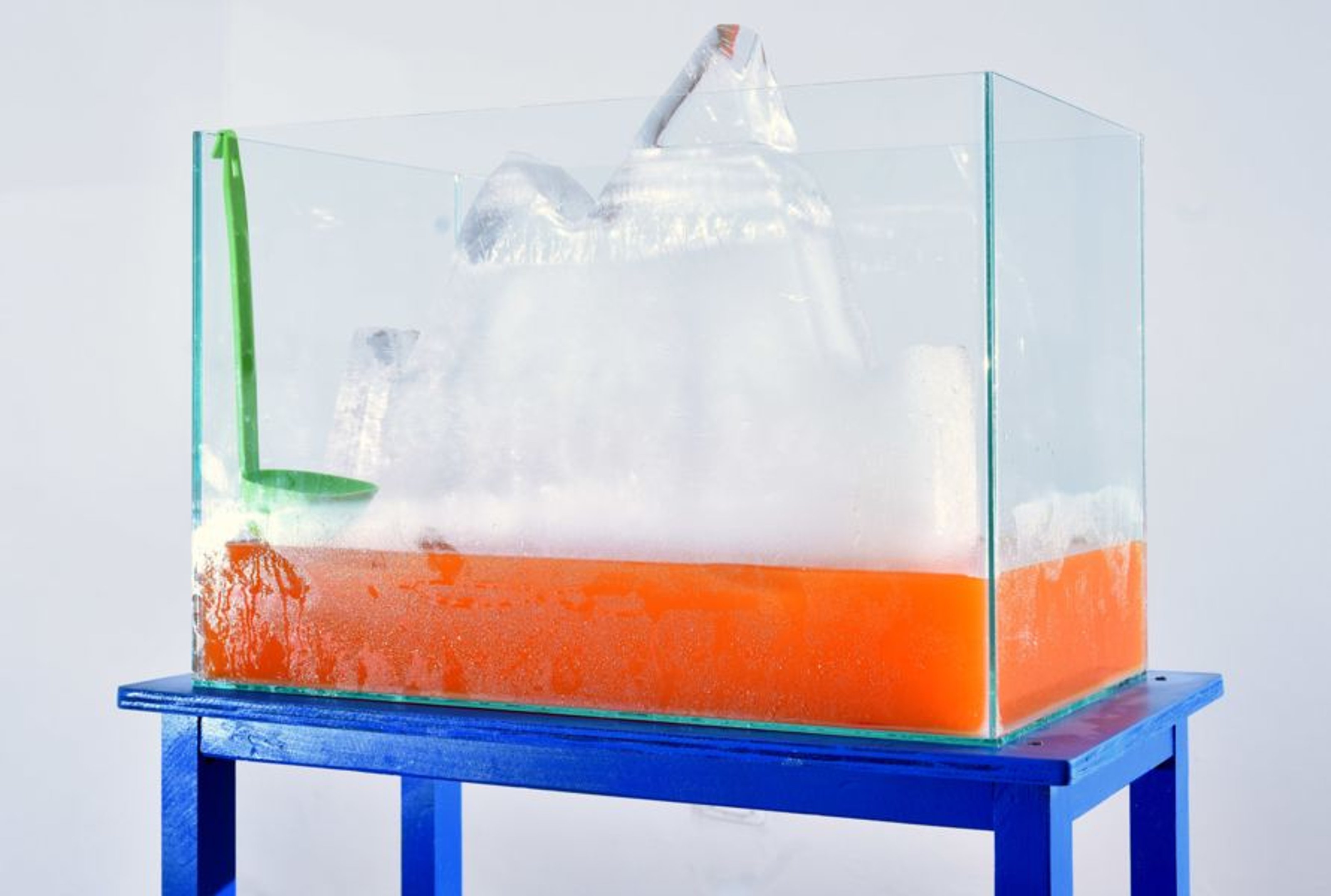 Ice in a water tank, with a red fluid under it and a ladel attached to the side