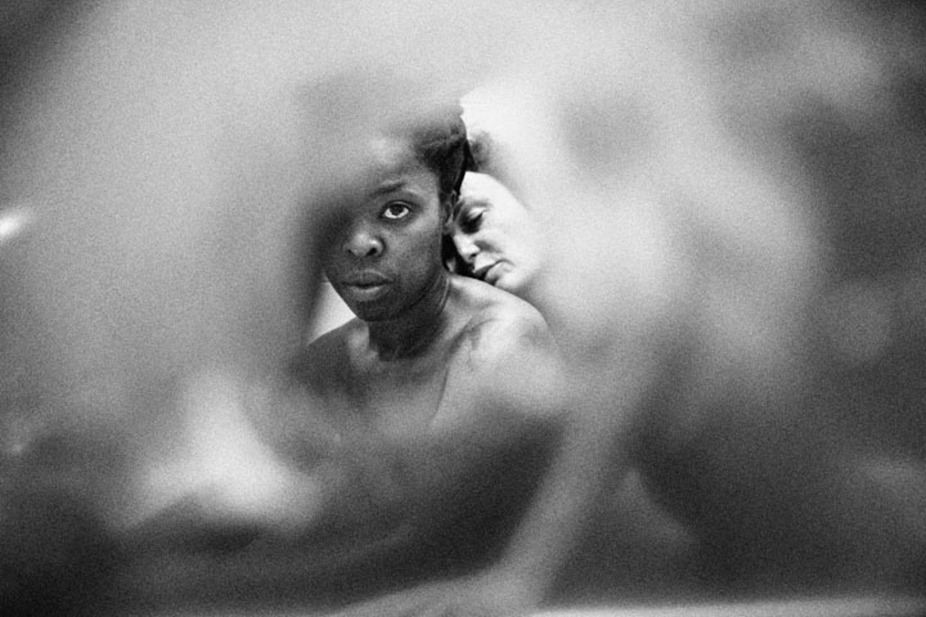 black and white photo, abstract circle centering Zanele Muholi and another woman lying on her neck from her back
