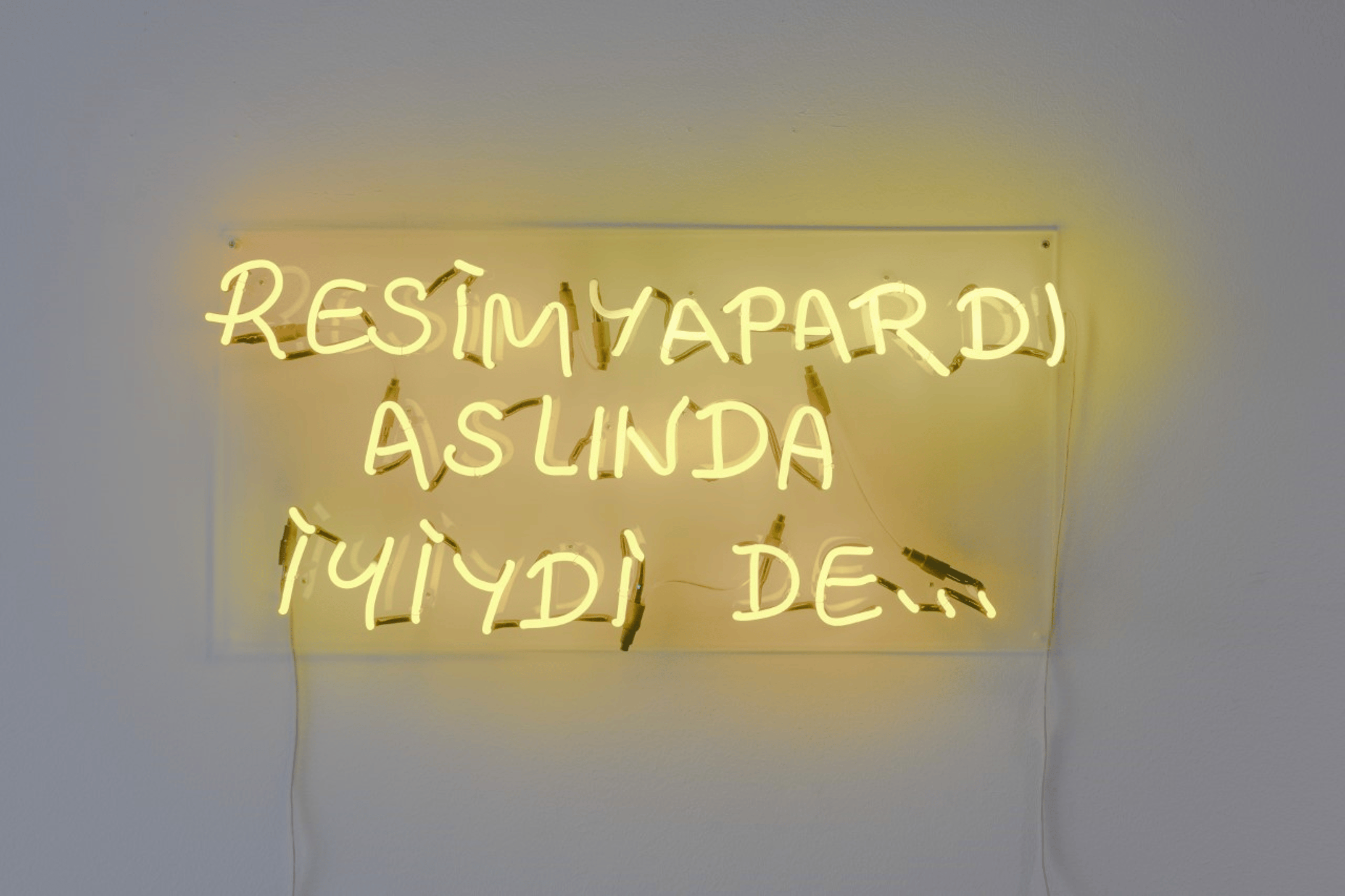 Ahmet Öğüt stands next to a neon work hanging on the wall in front of a group of museum visitors.
