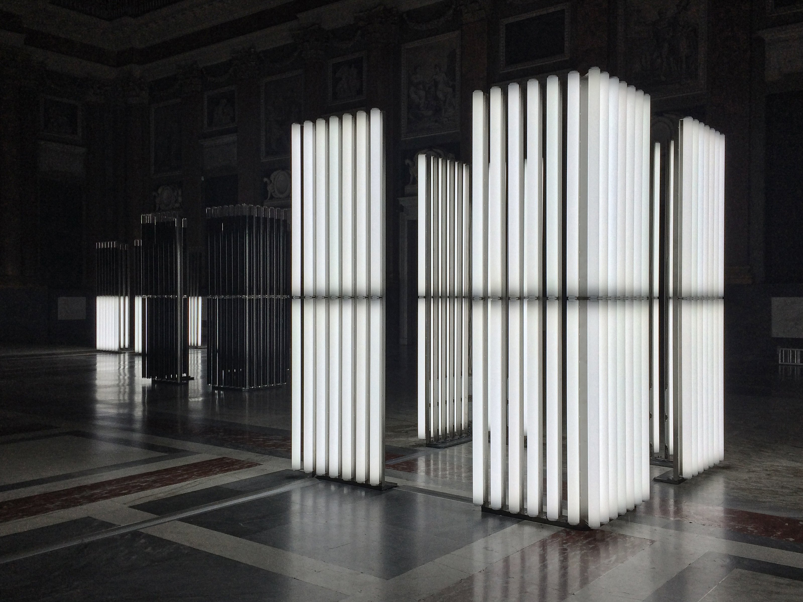 Neon industrial tubes filled with white-colored oil in dark space with black floor resembling iron bars.