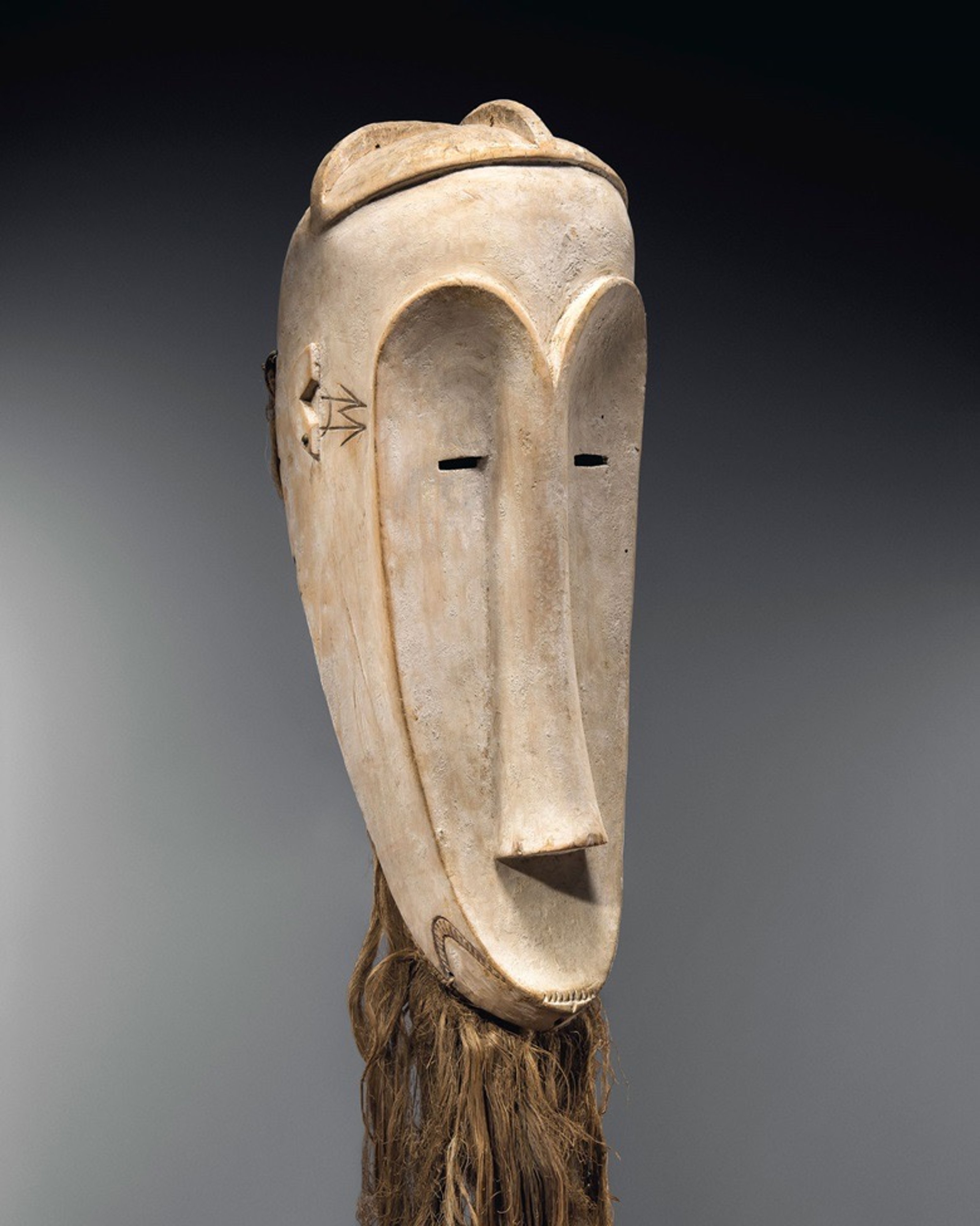 An off-white Ngil mask with a brown beard, characterized by its length.