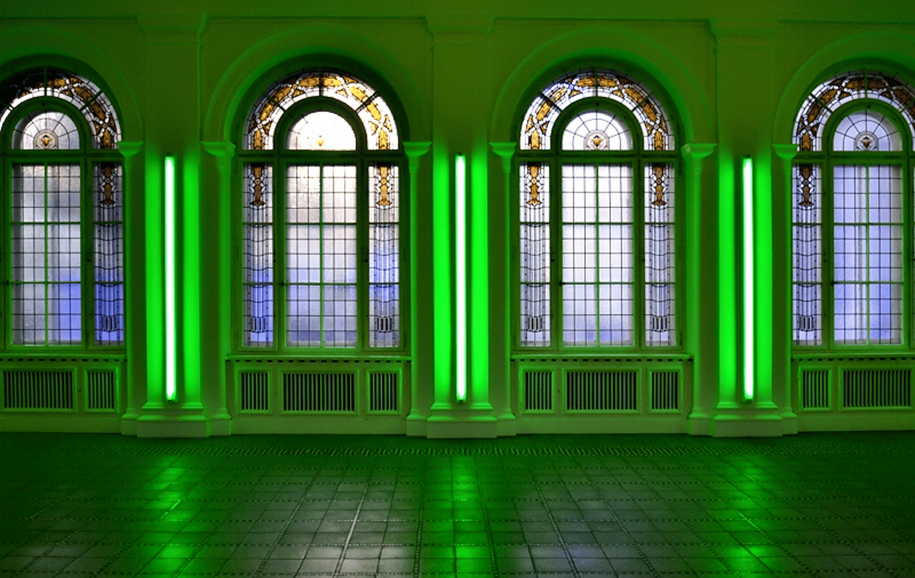 The lights are green neon lights mounted vertically on the wall between the patterned windows.