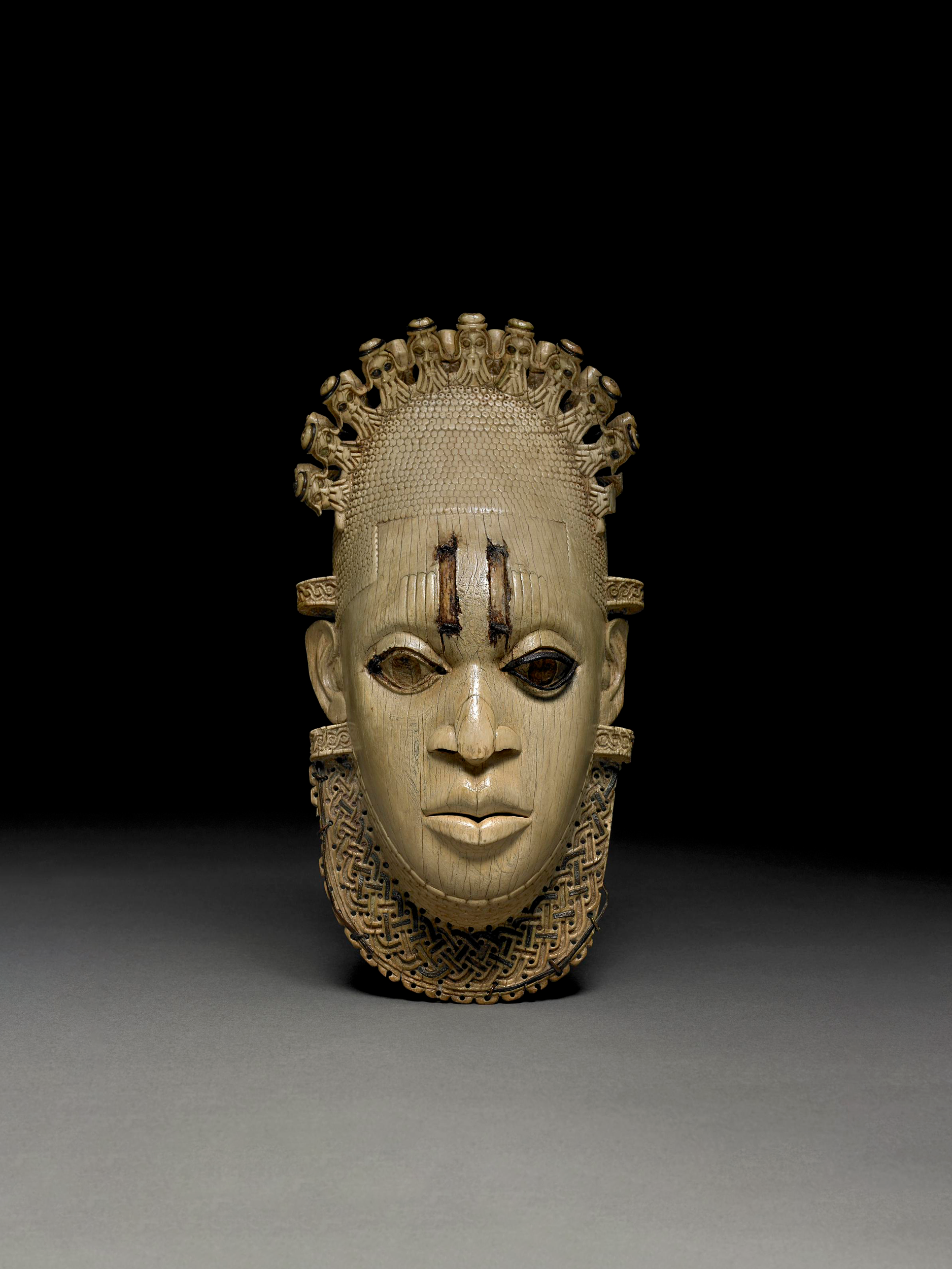 Wood carved look pendant mask outfit in front of a black background.