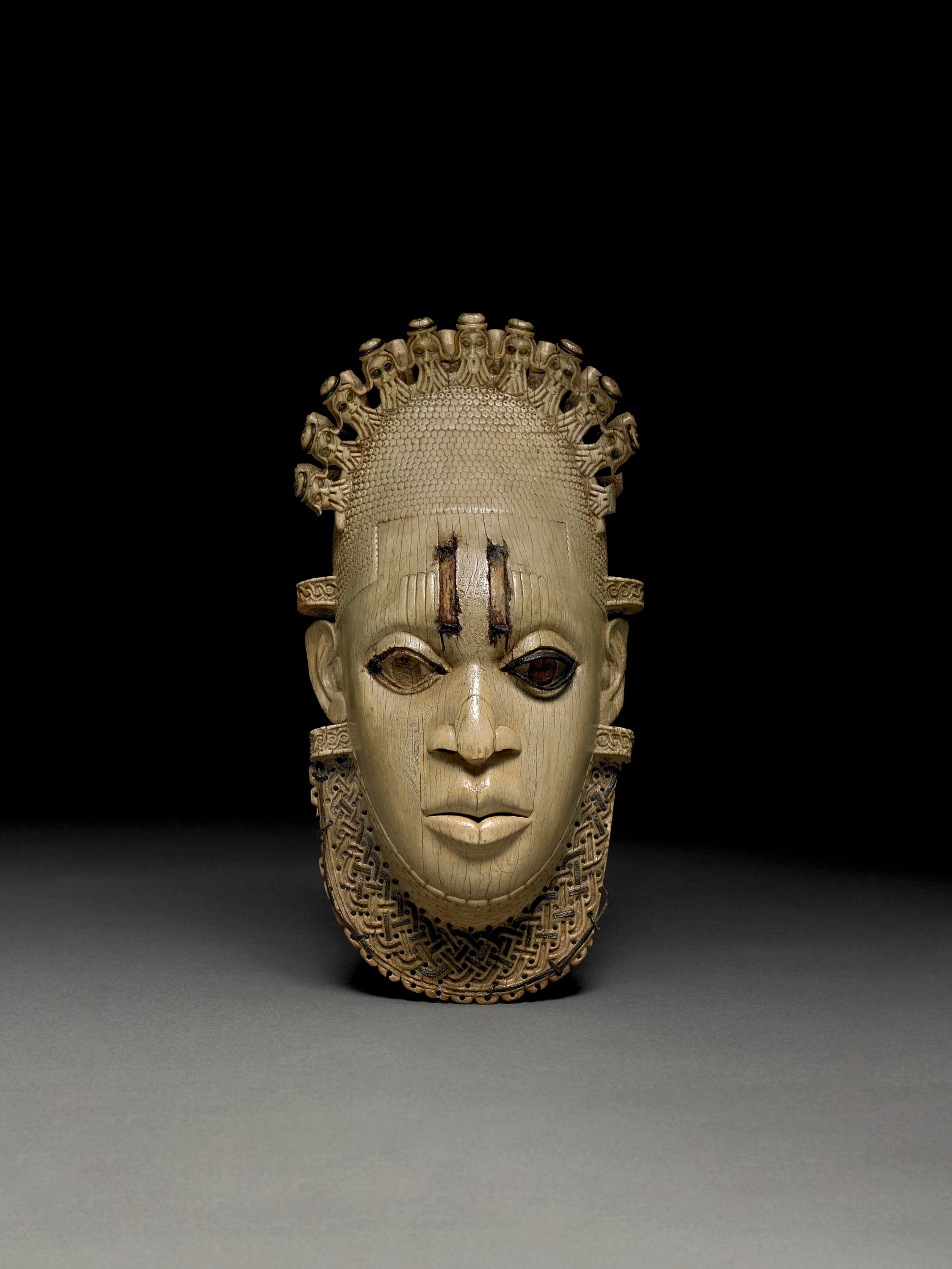 Wood carved look pendant mask outfit in front of a black background.