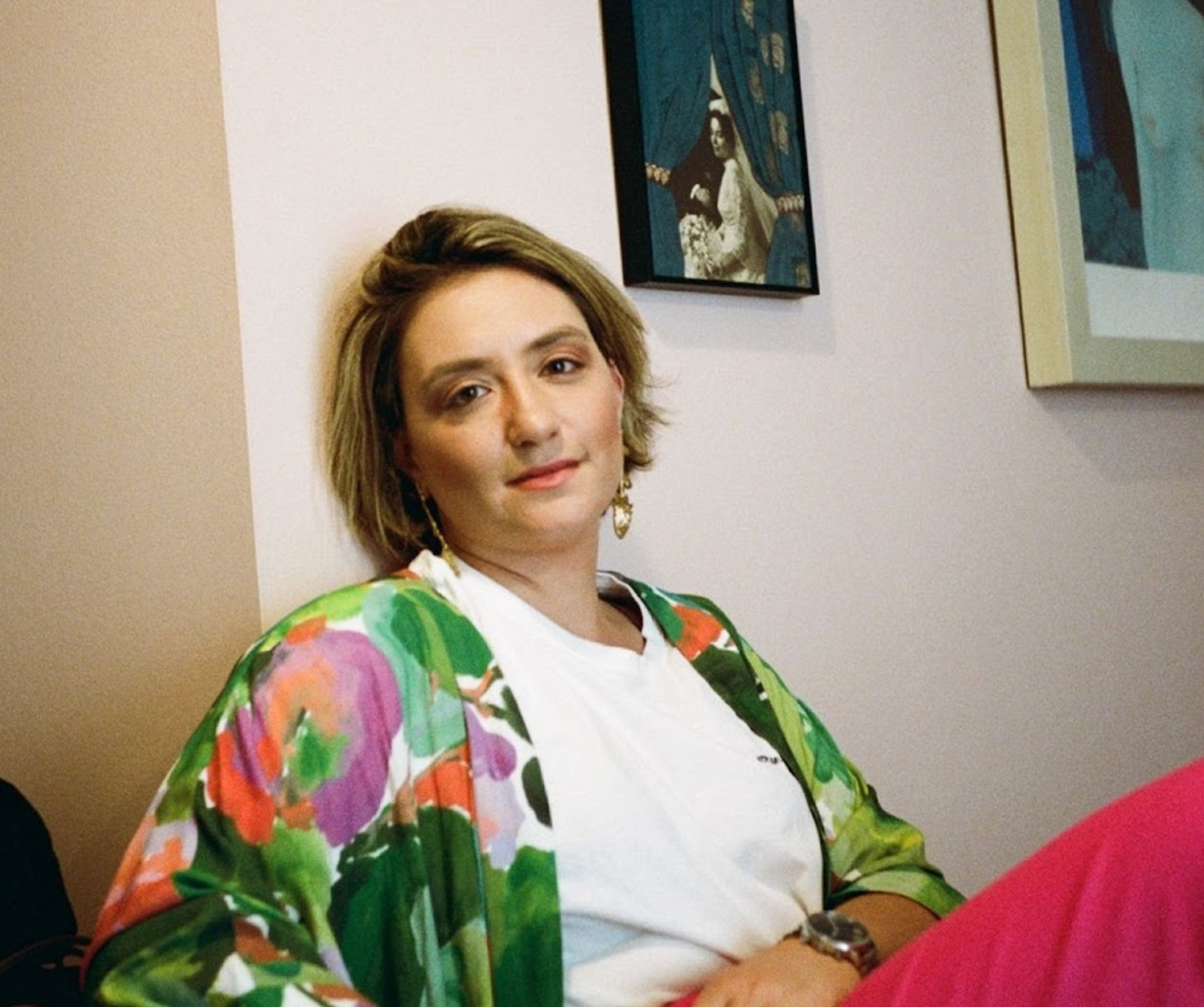 Huma Kabakcı sitting in front of beige wall with green painting, wearing floral shirt.
