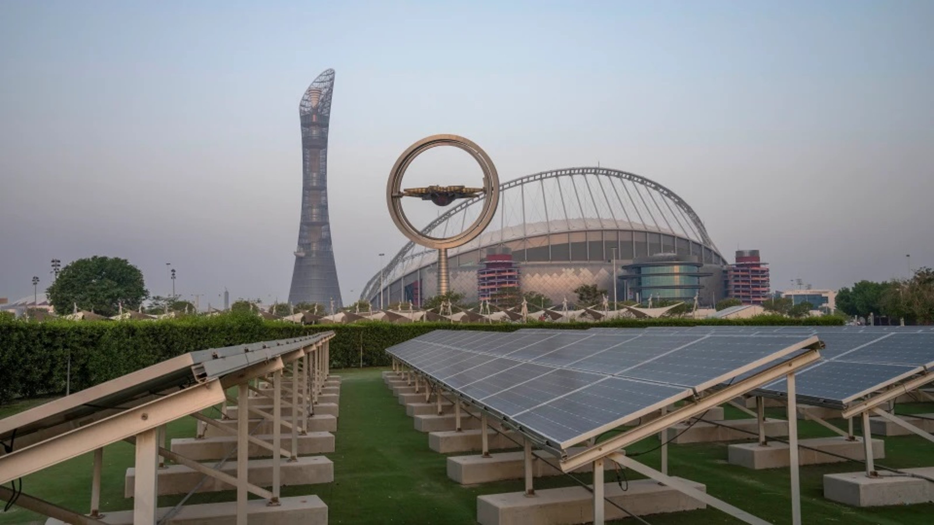 A row of solar panels and the huge Khalifa International Stadium behind it.