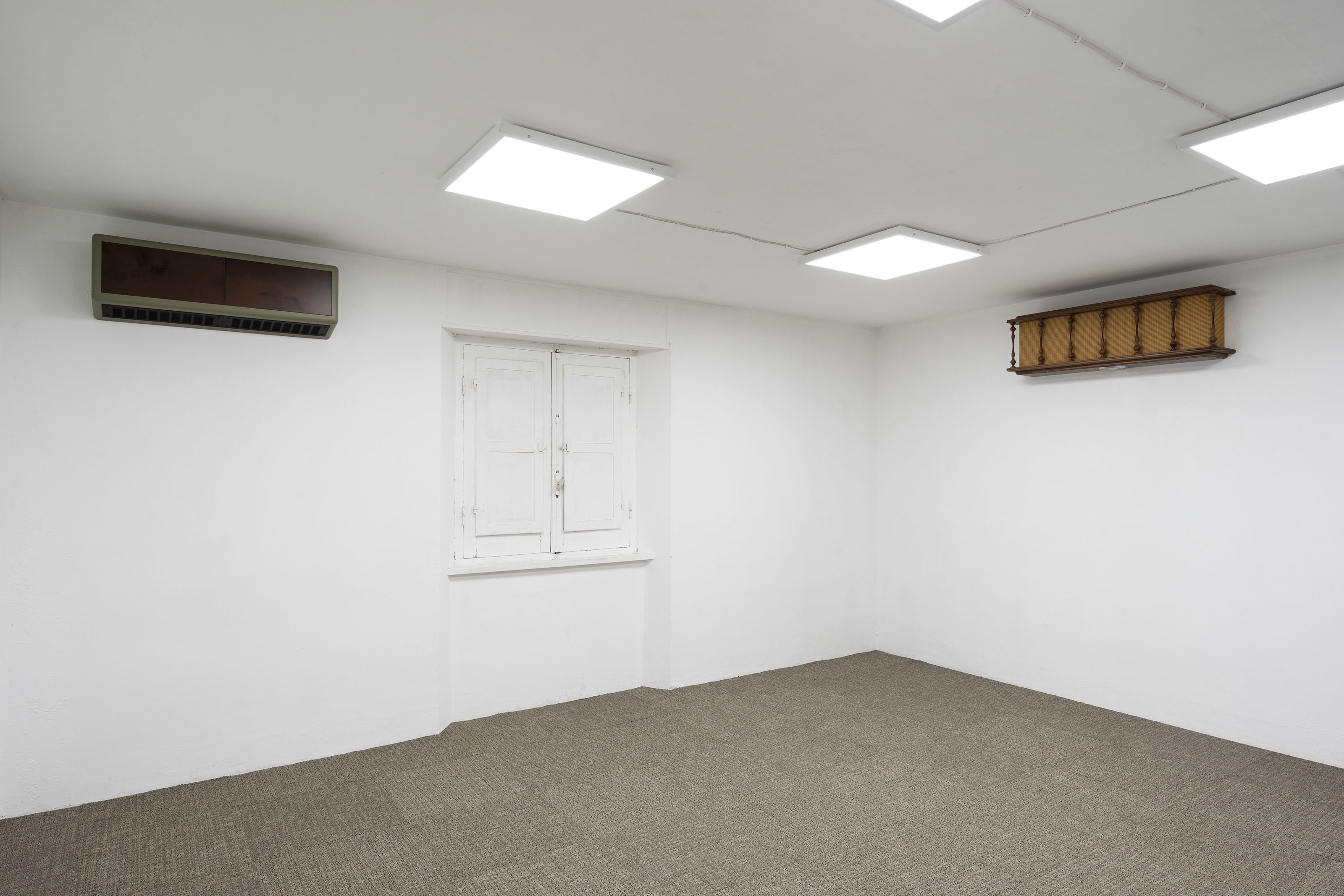 Two rectangular objects hanging on the walls of a room with white walls, gray carpet, illuminated by white lights.