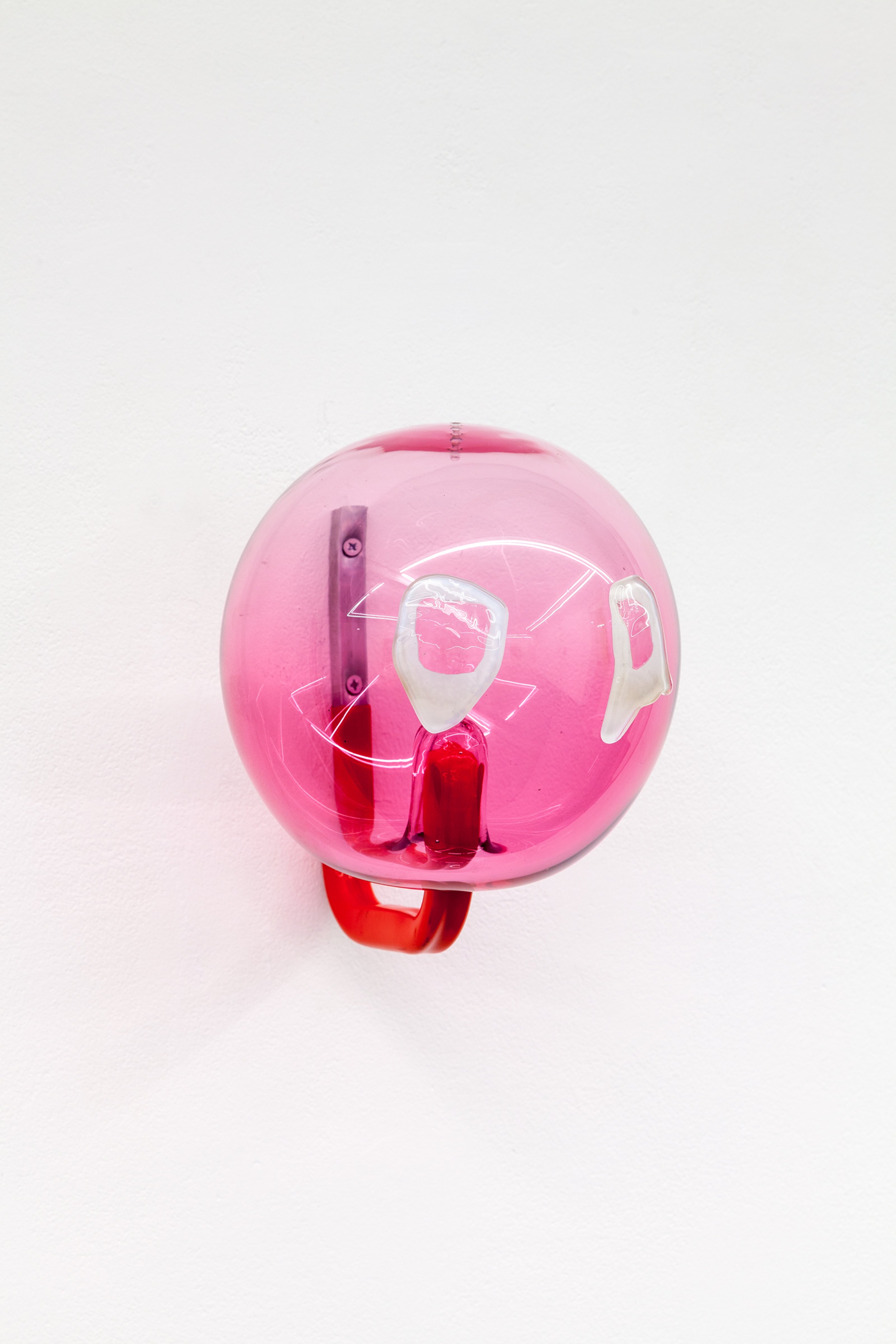 A pink sphere made of glass is mounted on a white wall via a metal hanger.