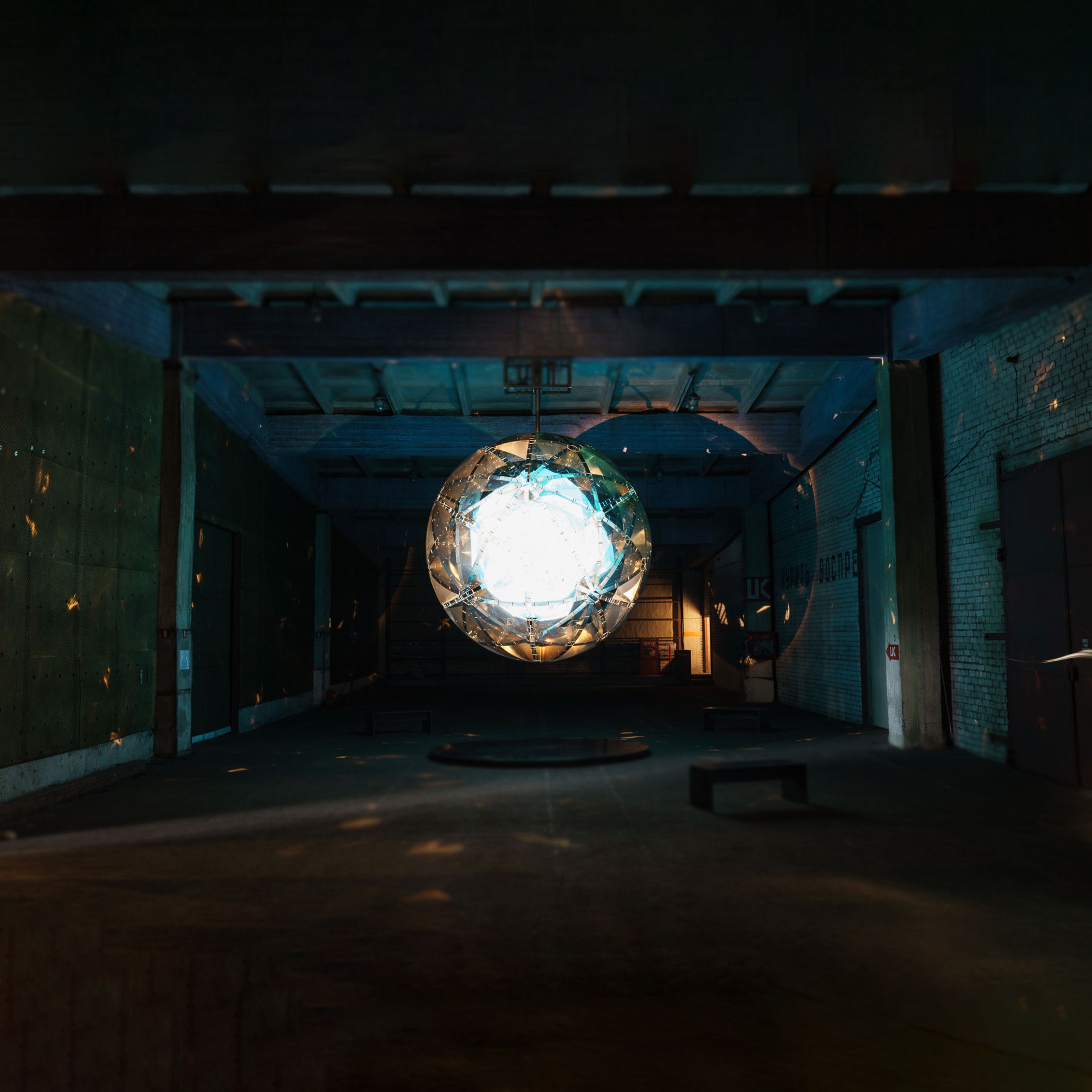 A gigantic glowing crystal suspended from the ceiling of a dark concrete room.
