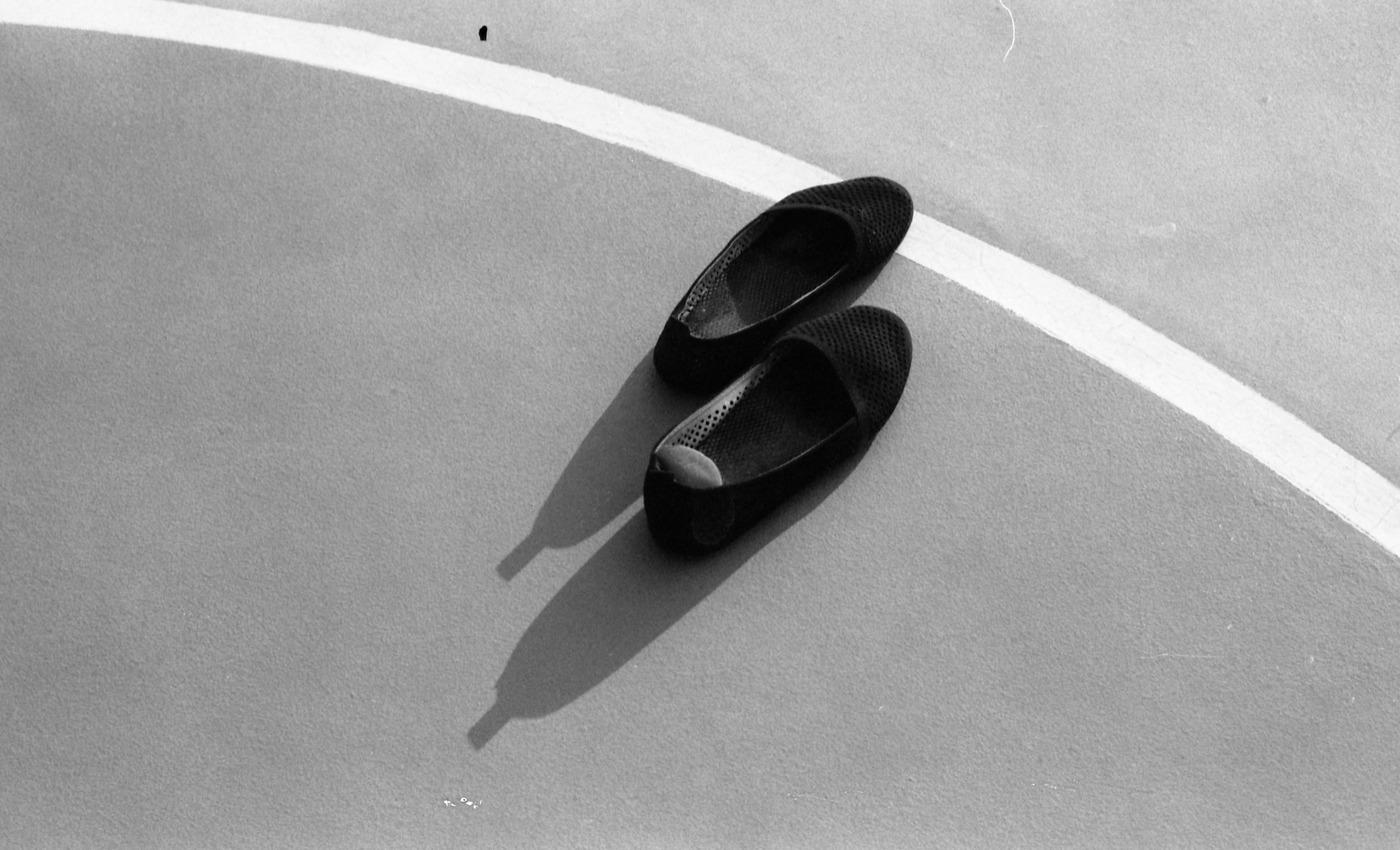 A pair of black ballerina shoes placed on a gray floor outdoors.