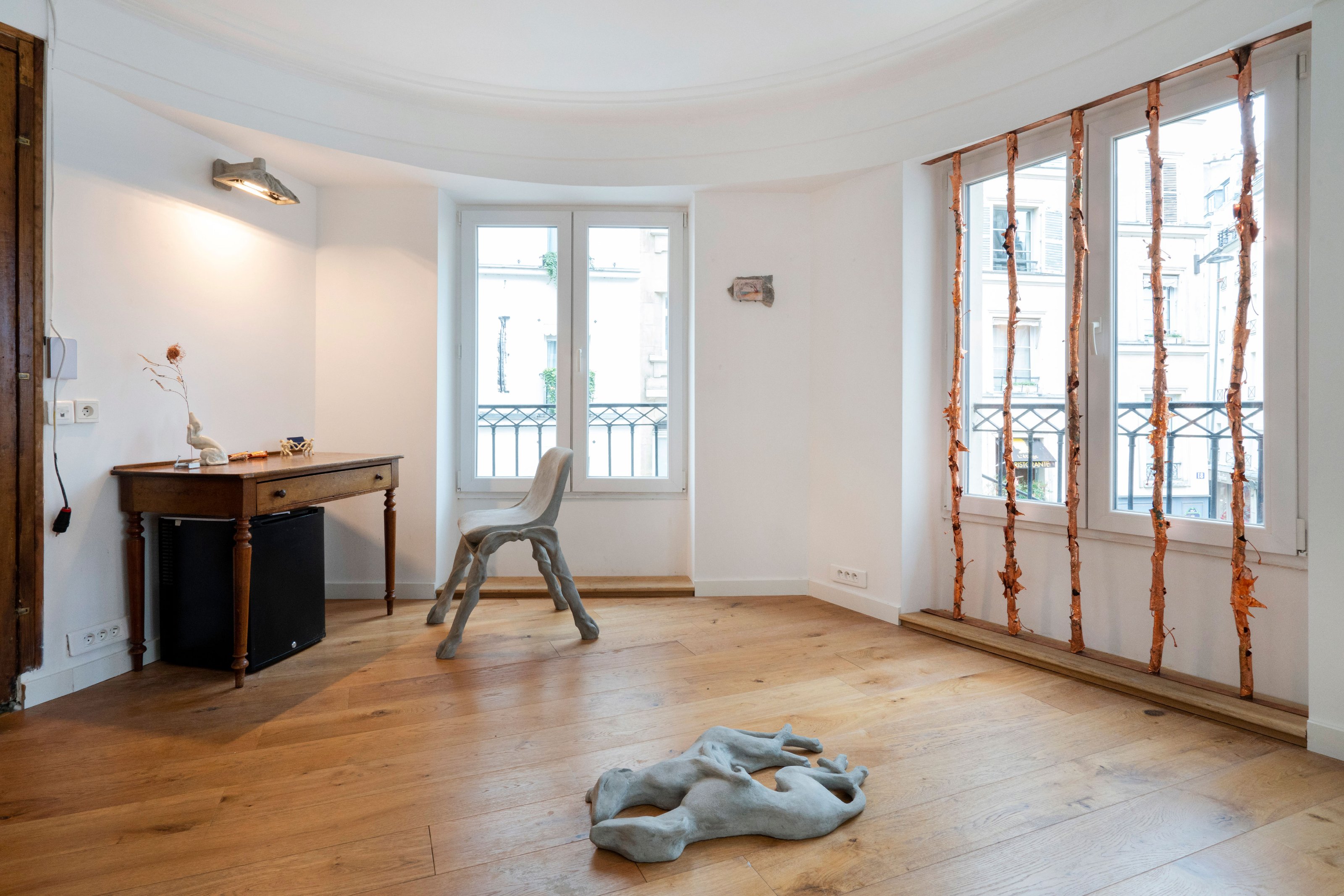 A specially designed table, chair, dog sculpture on the floor in an art gallery with wooden floors and white walls.