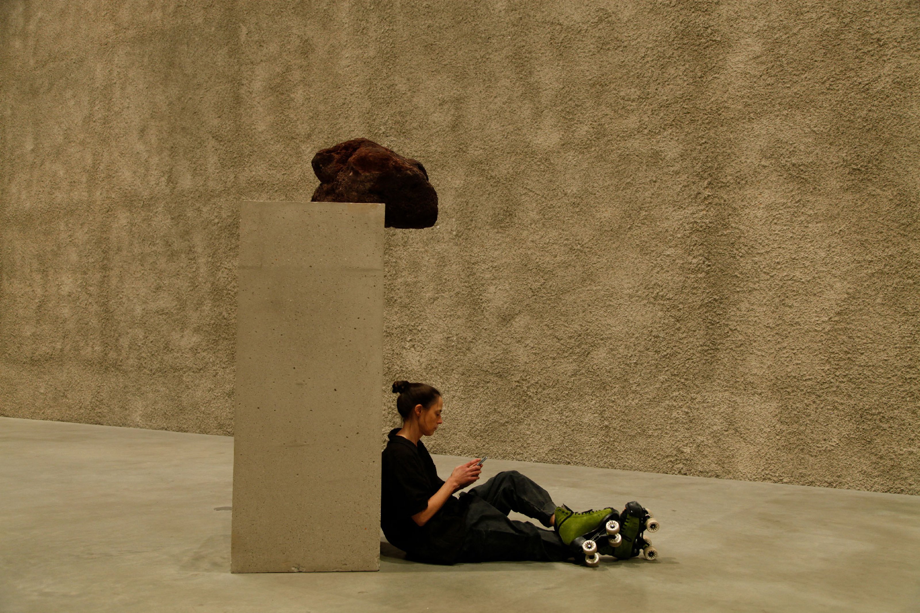Alexandra Rothert, sitting with her skates on, leaning her back on a pillar in the gallery space