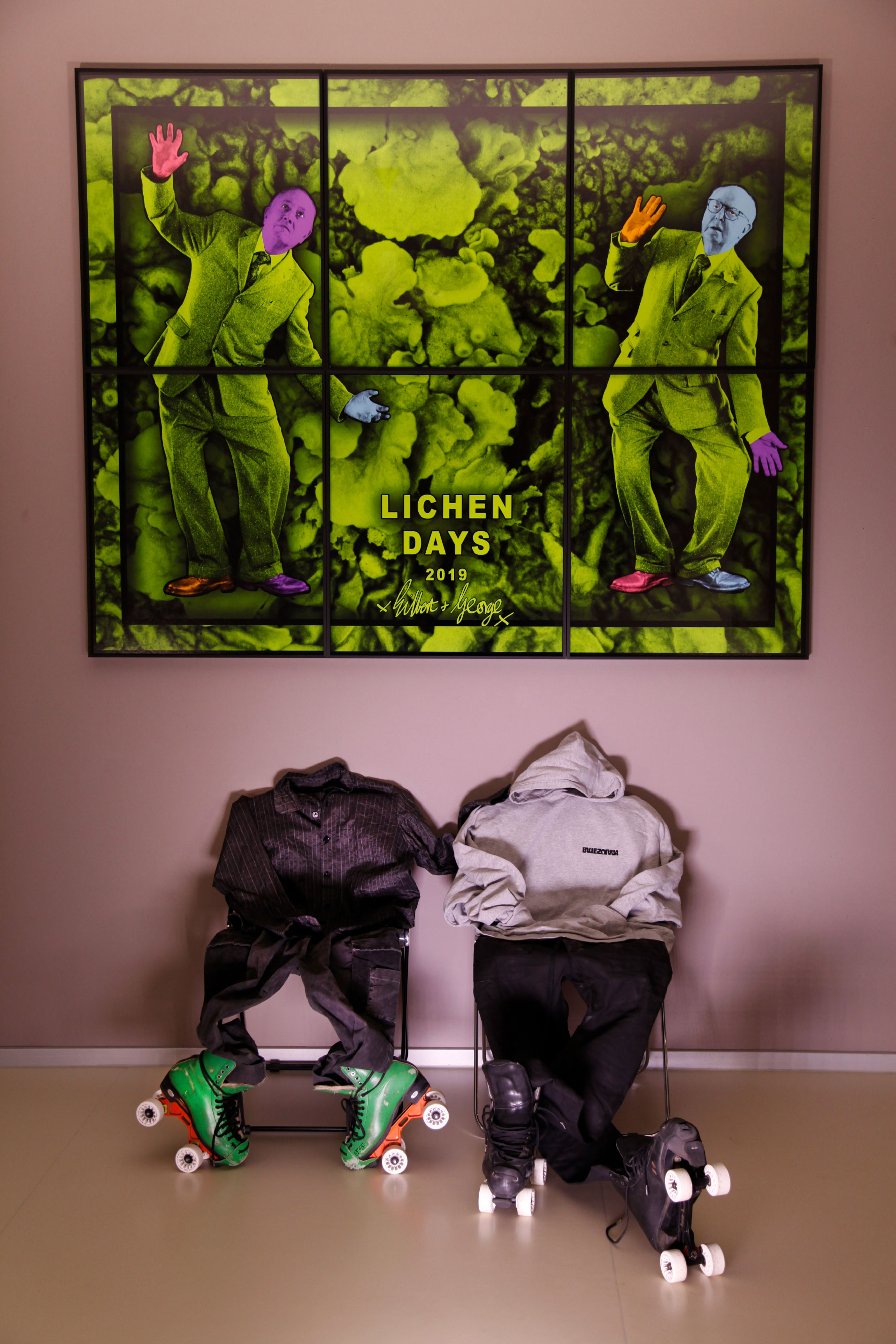 Two chairs standing under the green painting hanging on the wall and skater clothes standing on the chair.