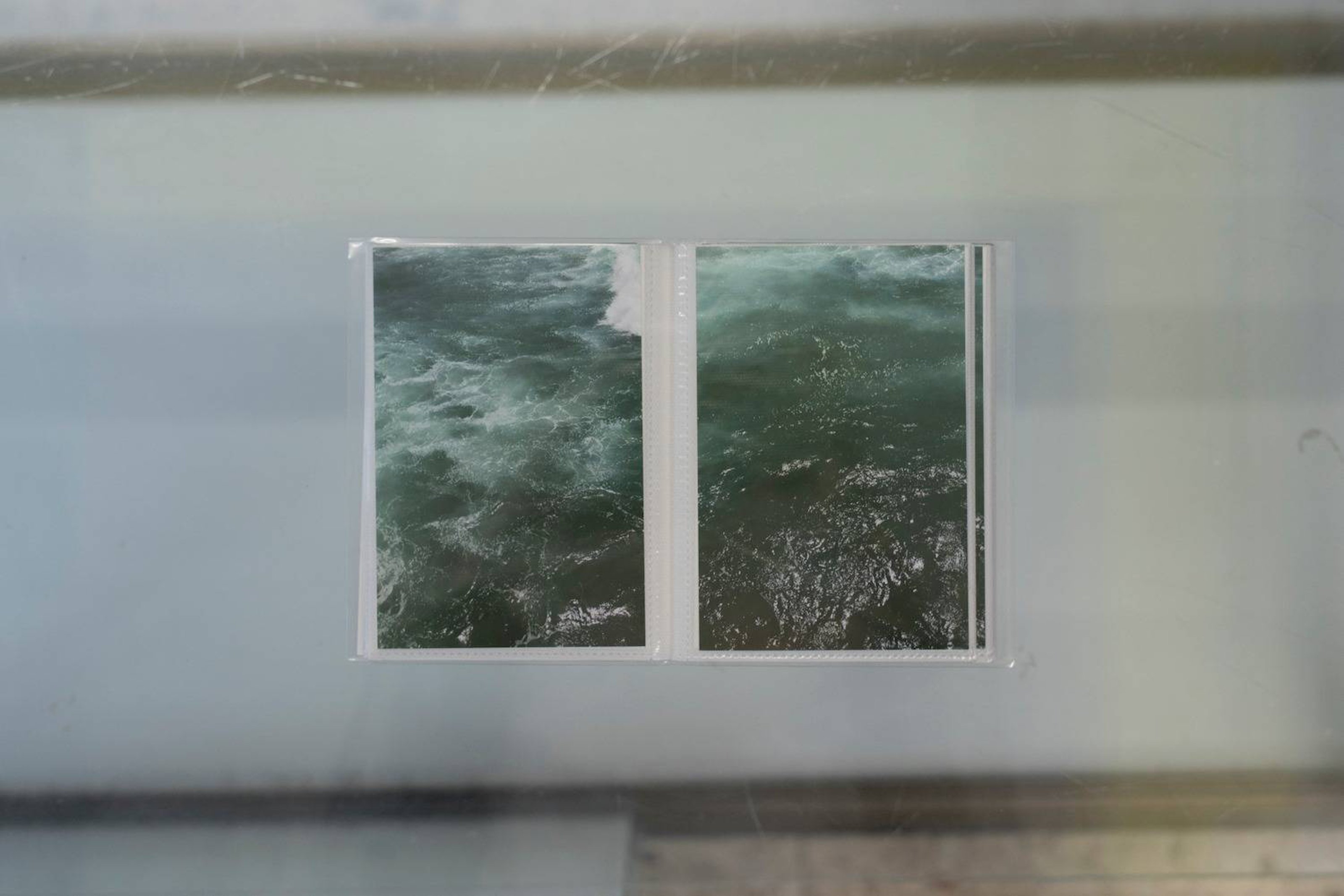 Photos taken from the sea are in a photo album, on a glass shelf.