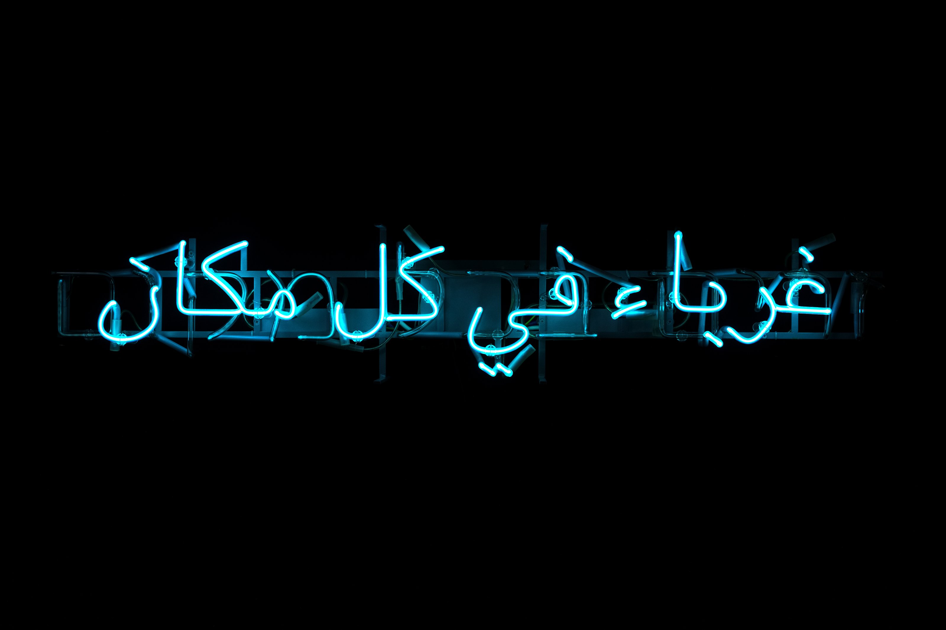 Neon blue text "Foreigners Everywhere" in Arabic part of Claire Fontaine's "Foreigners Everywhere, 2010" artwork.
