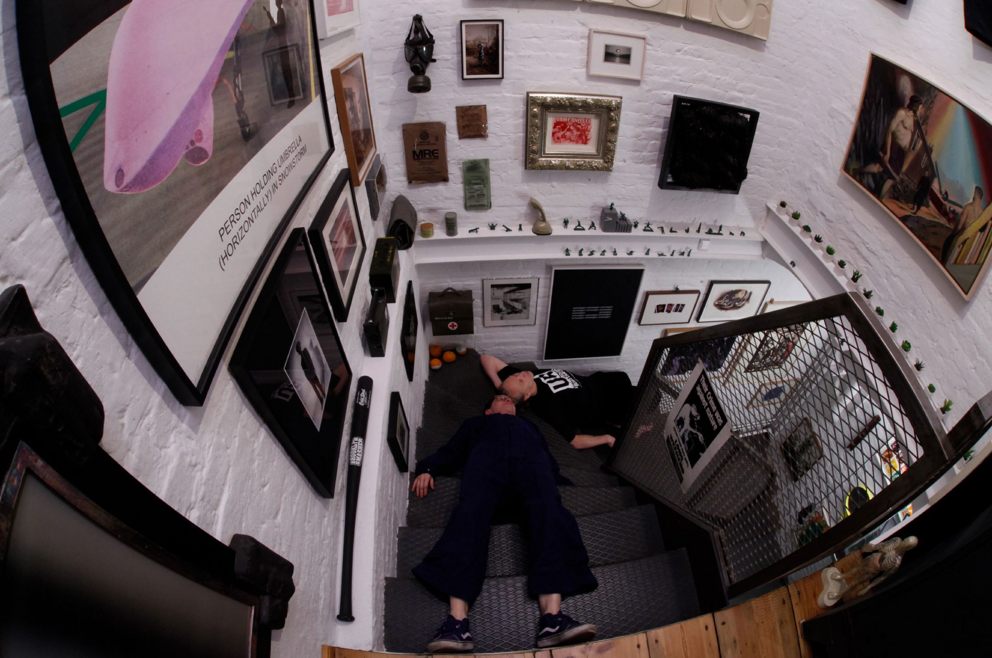 The couple lying down on the staircase. There are framed artworks on the wall surrounding them.