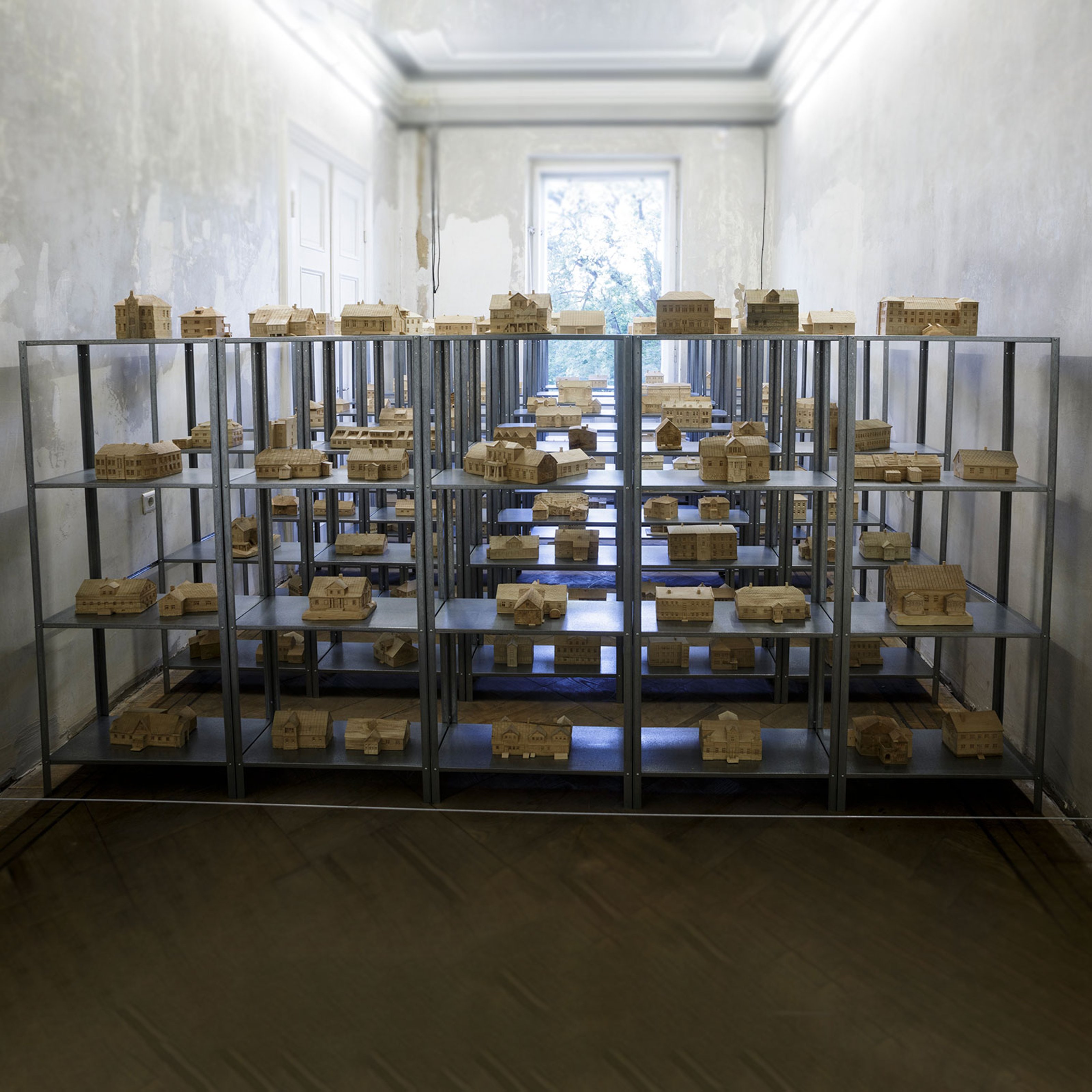 Models of stone buildings on metal shelves filled in an old, concrete, narrow space with one window.