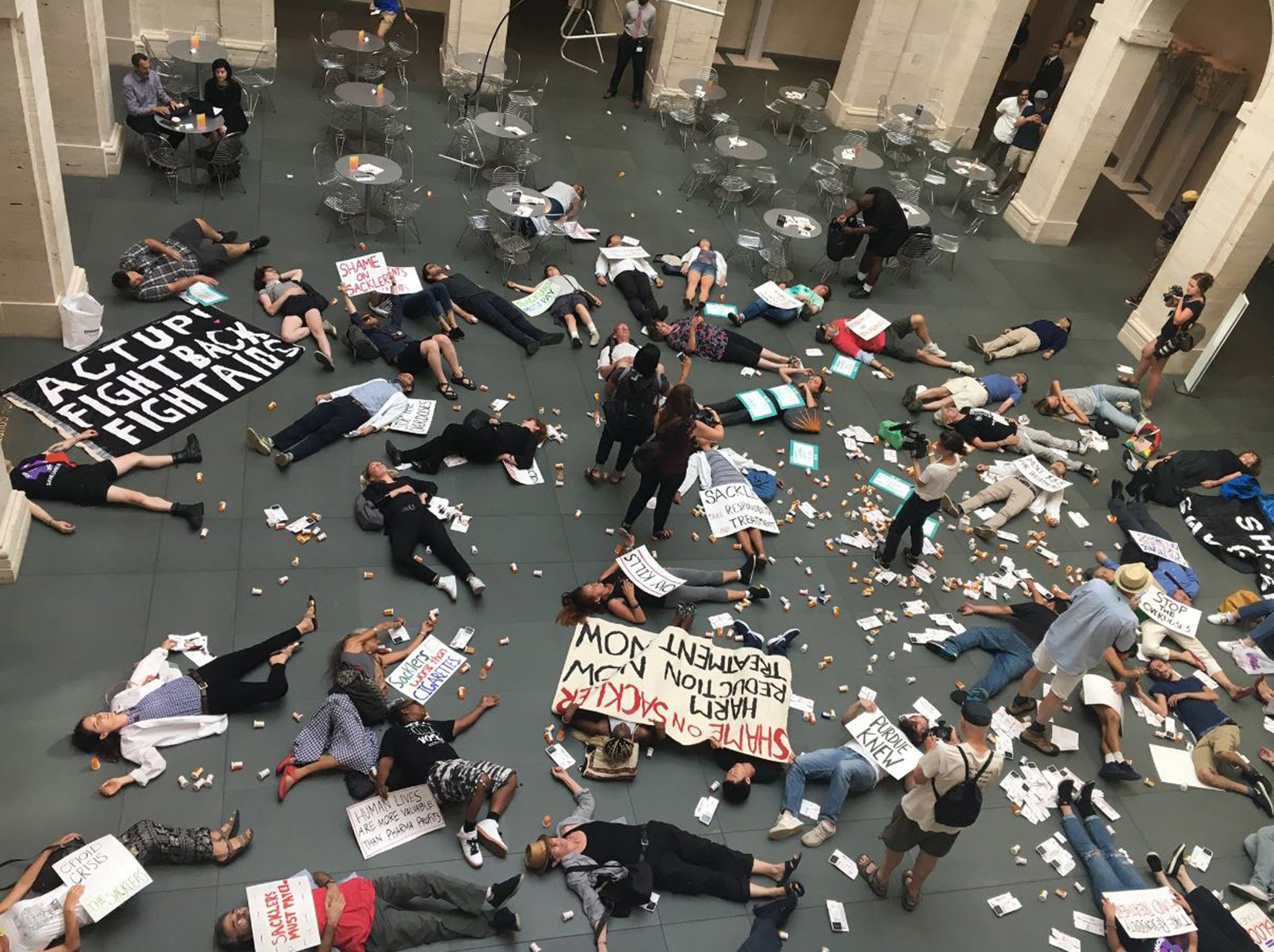 Protestors lying on the ground of a museum floor, signs that say: 