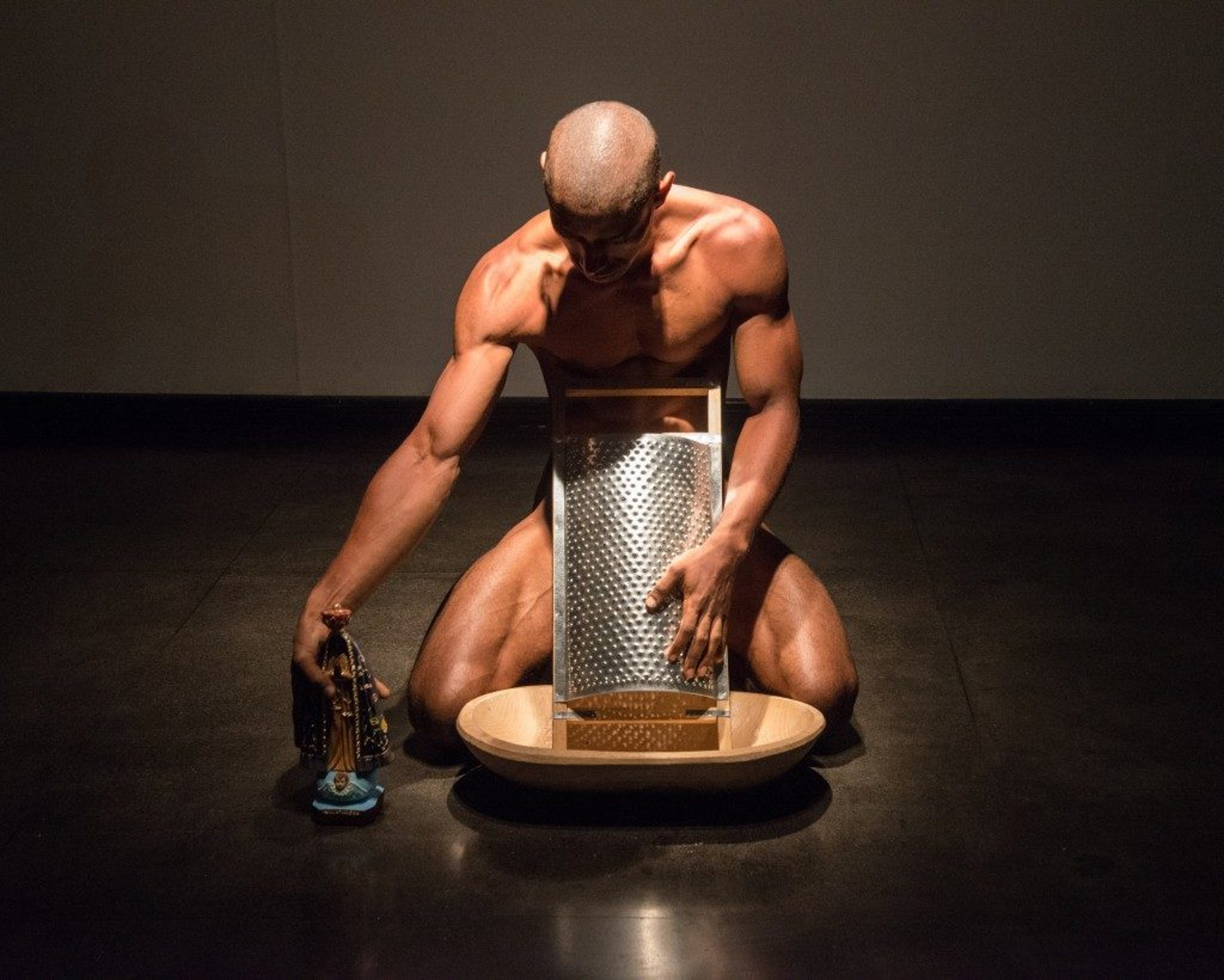 The artist grinding a statue of Virgin Mary and pouring the powder over his body.