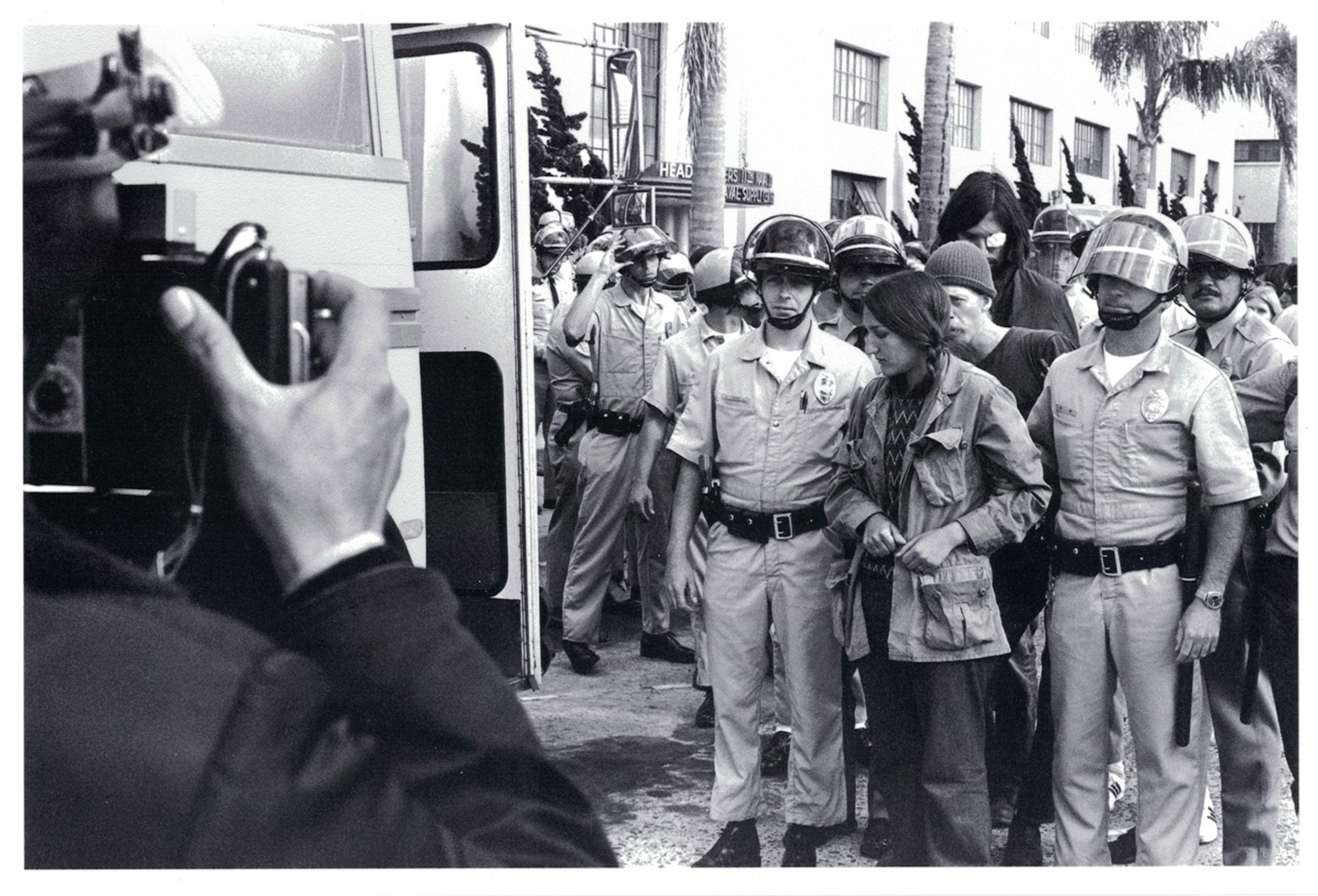 Photograph of a woman getting arrested in a Vietnam rally, next to a police van