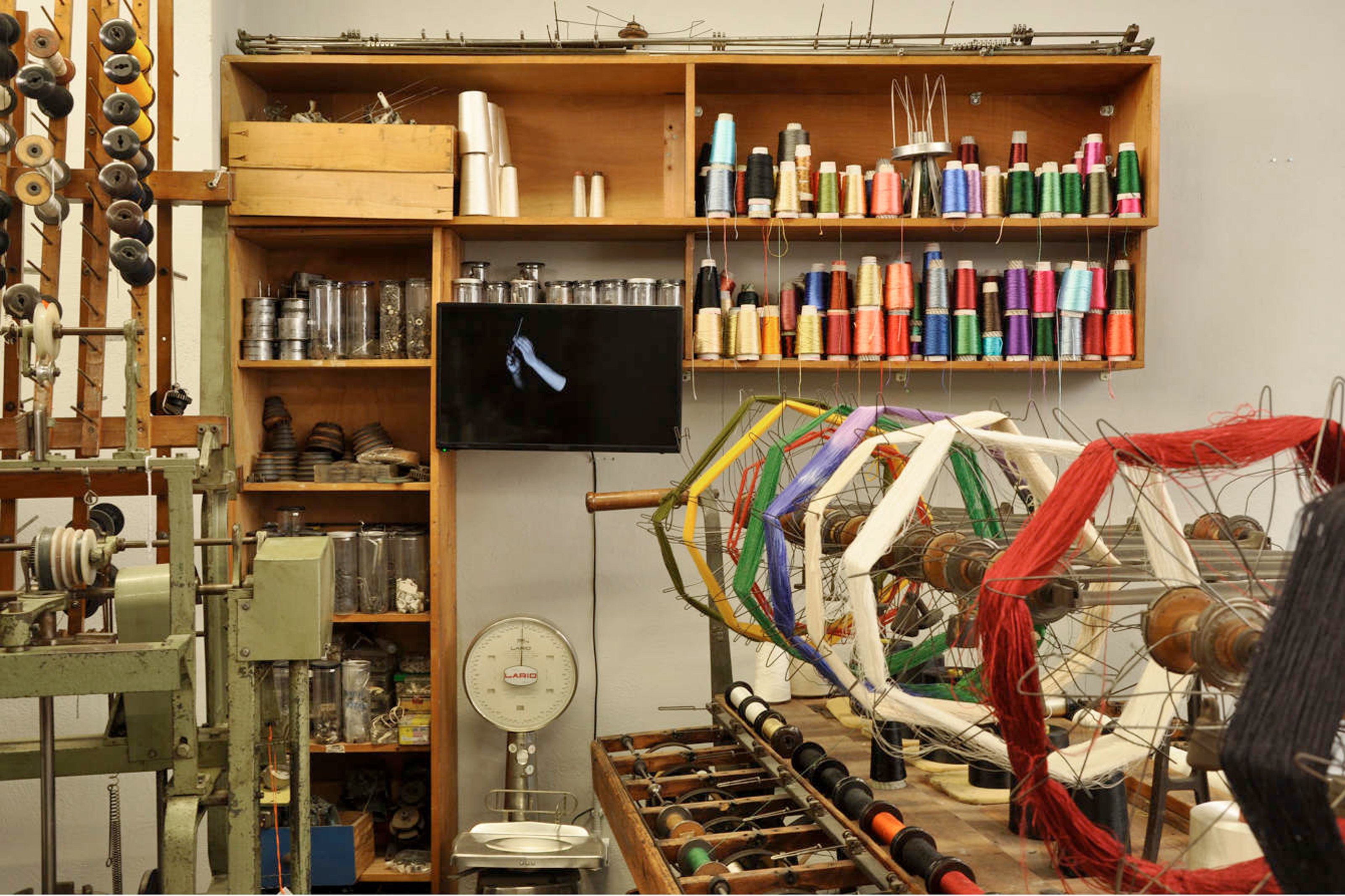 Threads and custom made loom on display, with a TV screen attached to a wall