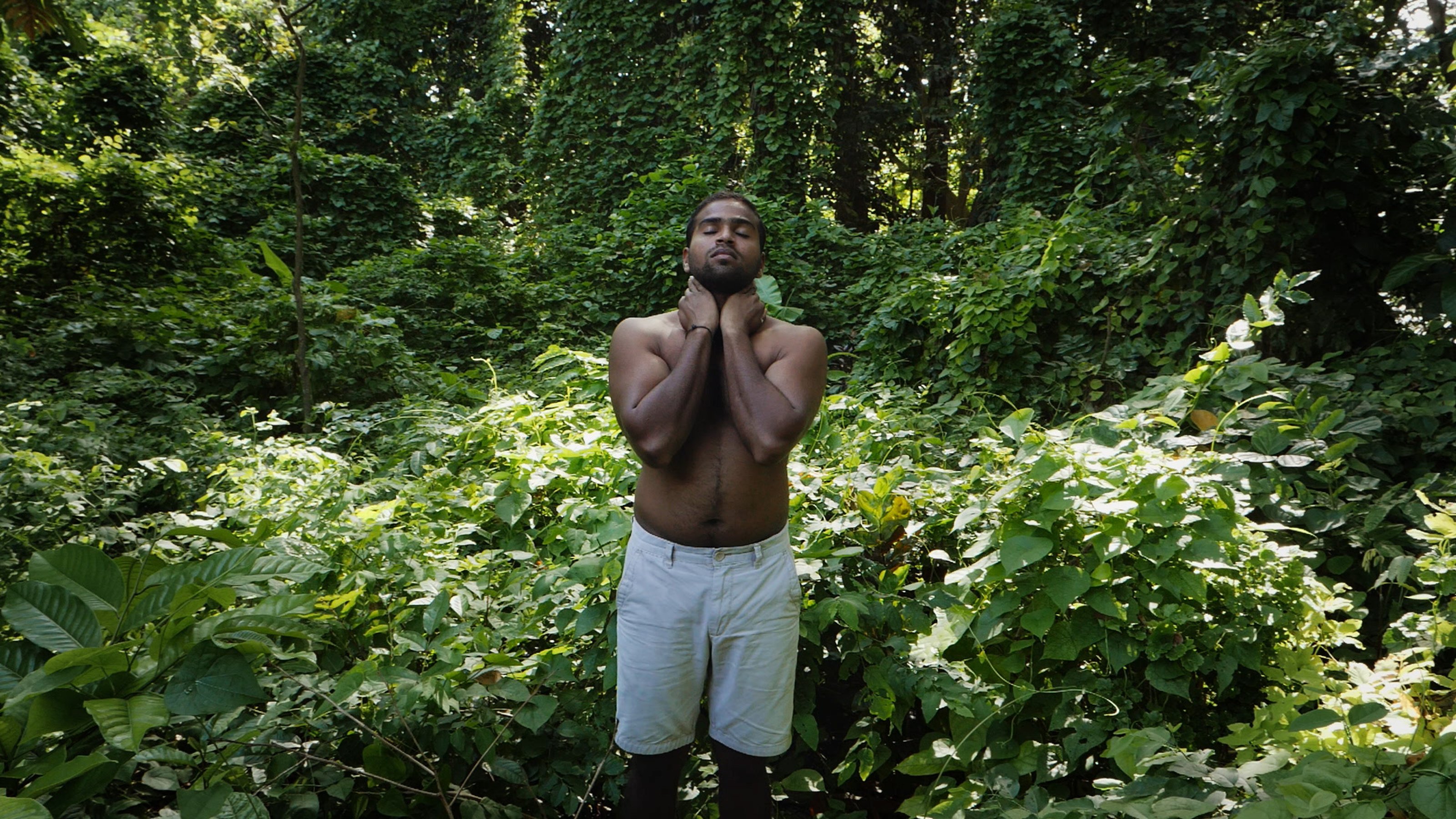 Man standing up, holding his neck with his head tilted backwards, in a forest