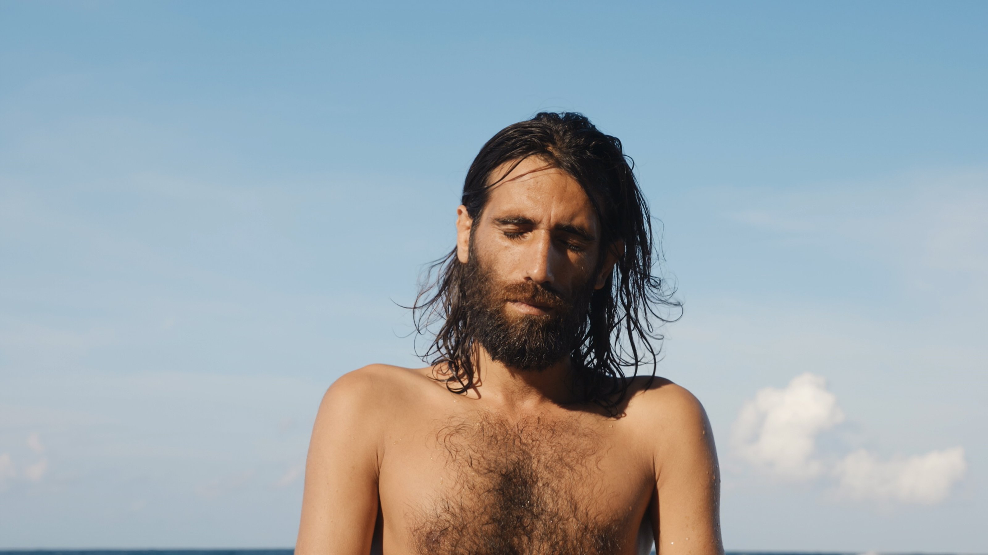 Close up of Behrouz Boochani with his eyes closed, on the beach