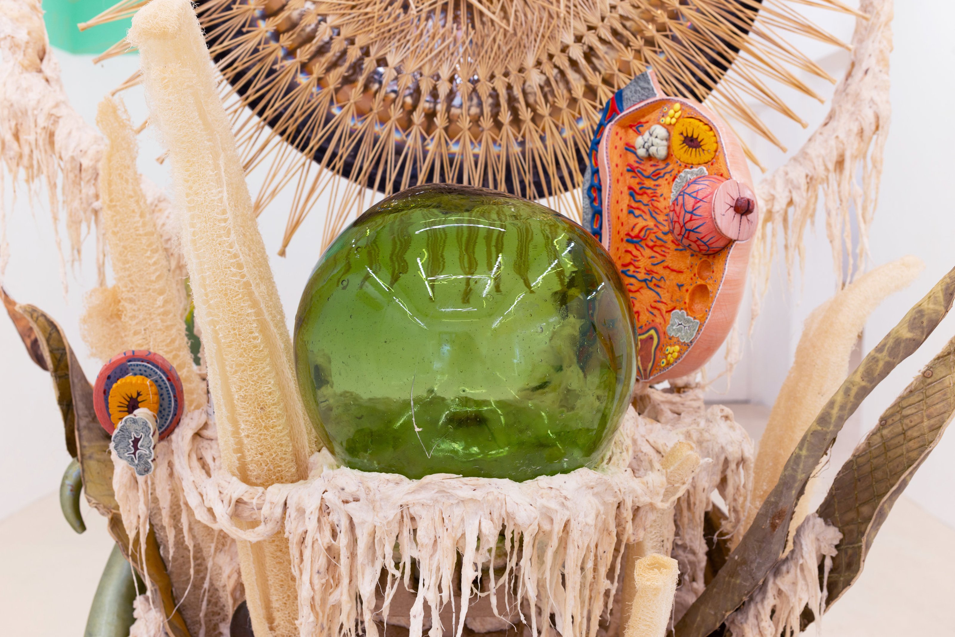 Detail of the sculpture, a green glass orb sitting on a platform, the materials around are organic and resemble body tissue