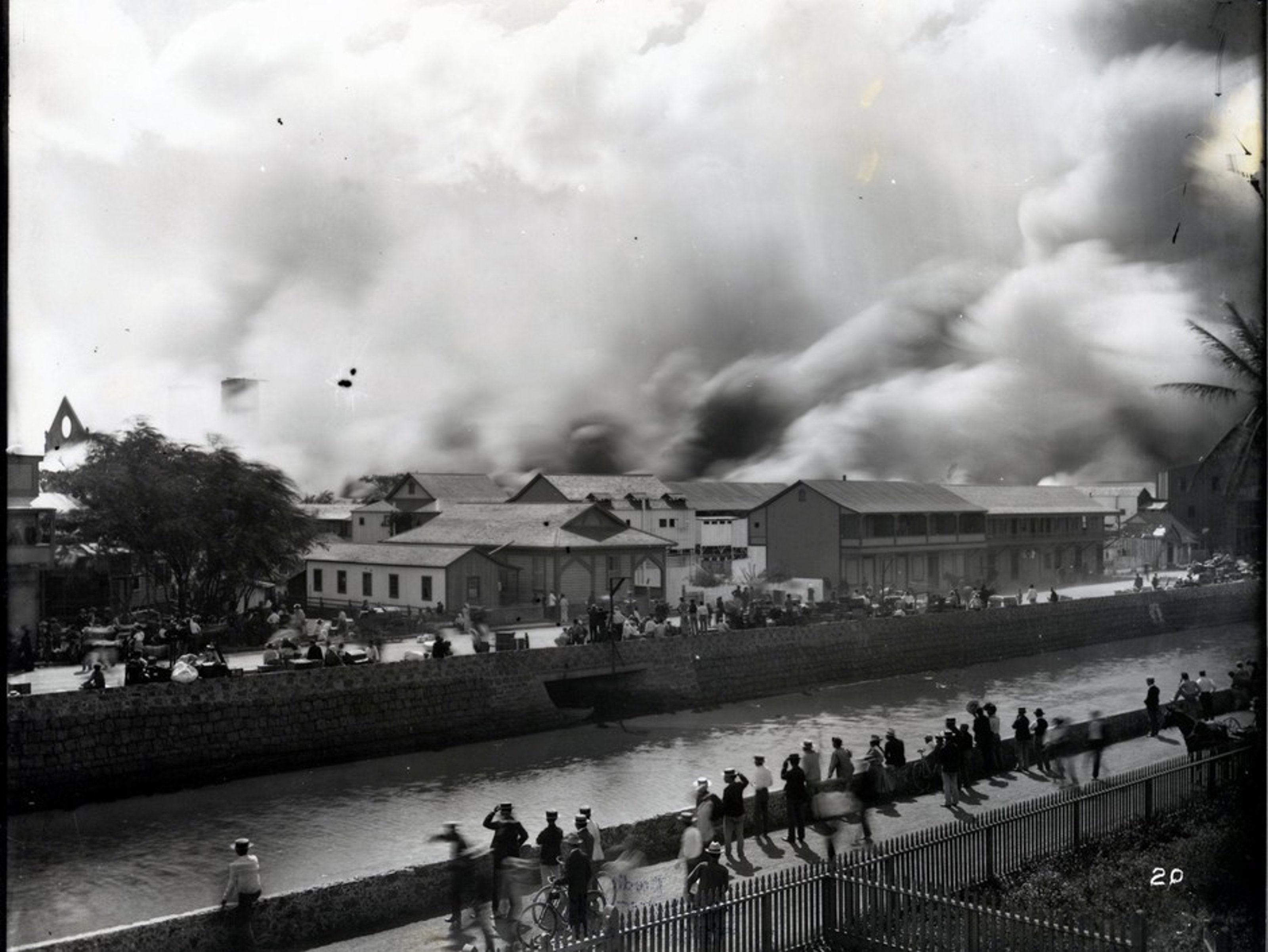 Smoke over Honolulu Chinatown, with a crowd watching on the other side of the river