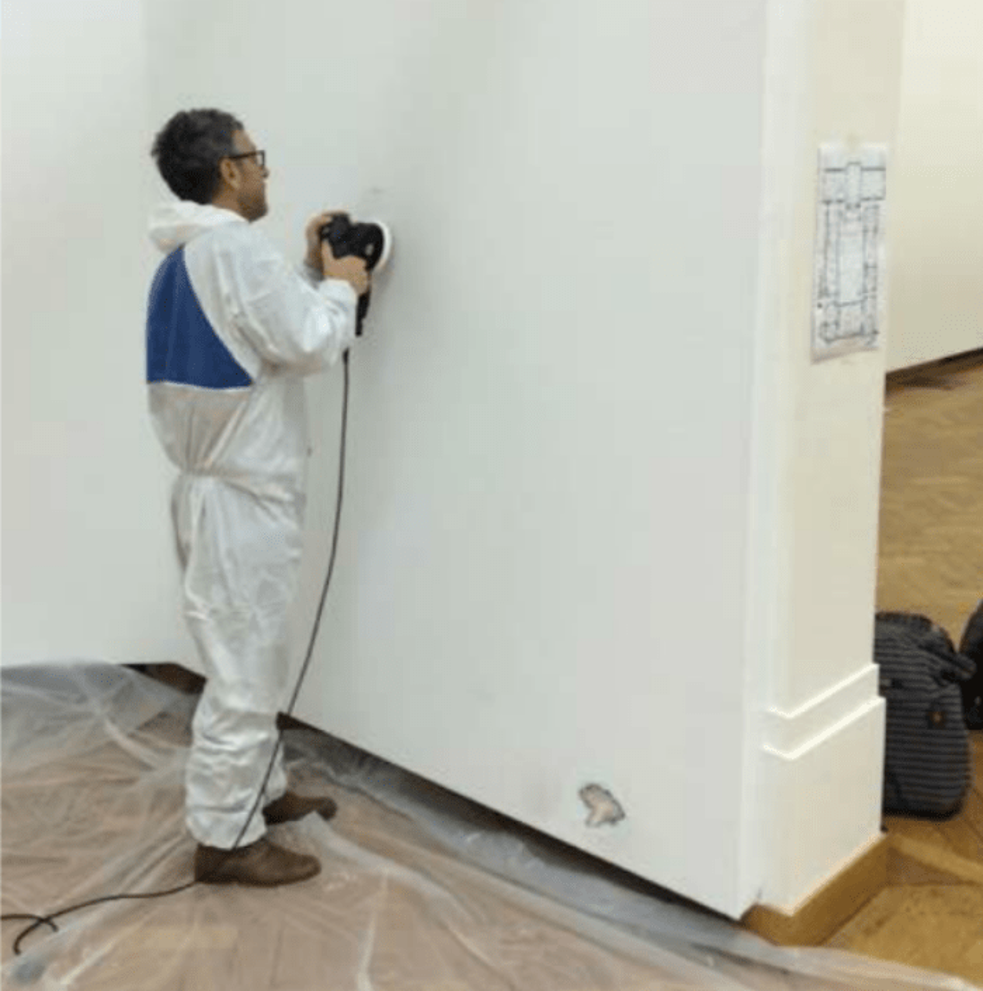 Pierre Huygue sanding a wall at the Palais des Beaux Arts, Brussels with an electric sander, dressed in all white