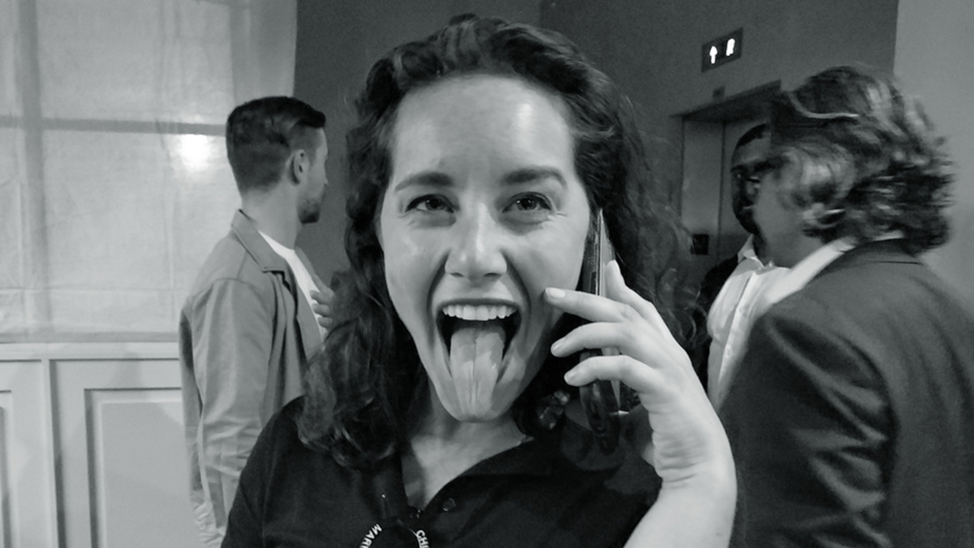 Black and white image of Ellie Rines sticking her tongue out while holding a cellphone to her ear