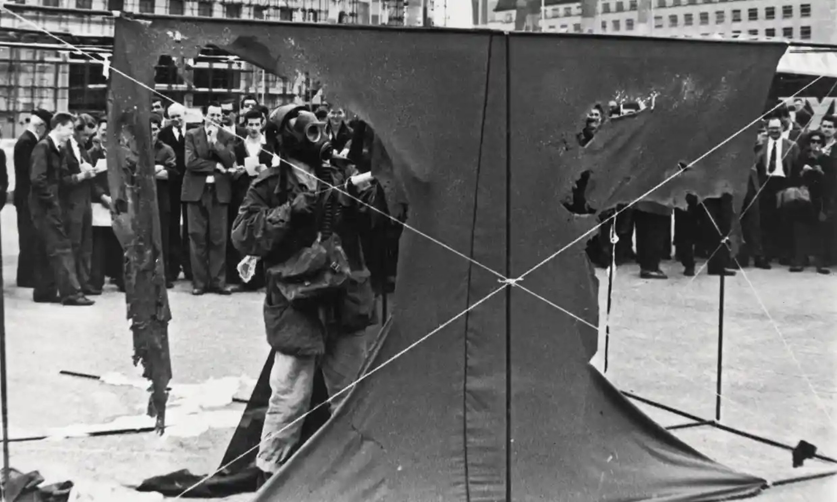 A man in militaristic gas mask and goggles, spraying hydrochloric acid on nylon sheets