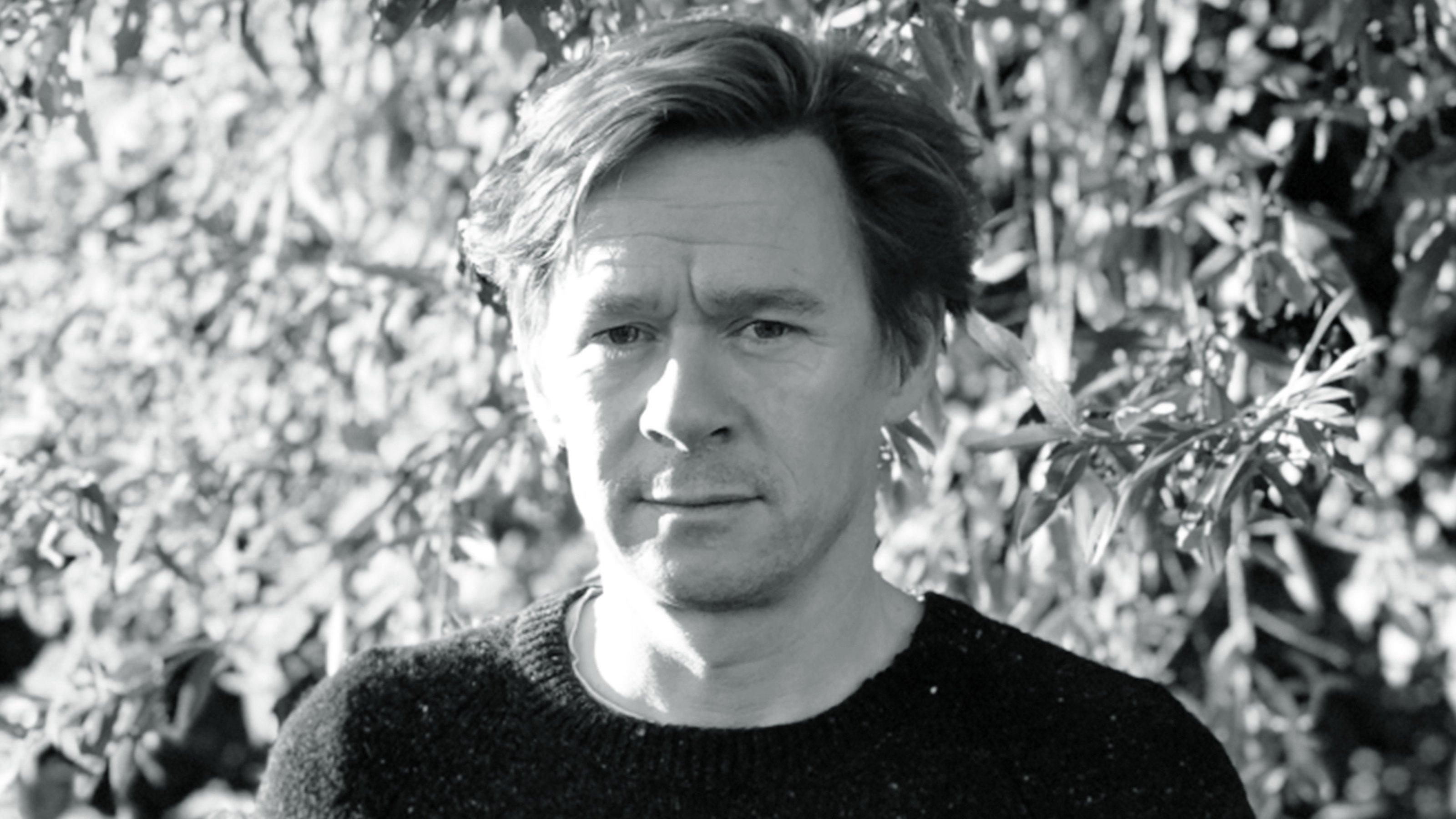 Black and white image of Kris Martin standing in front of greenery