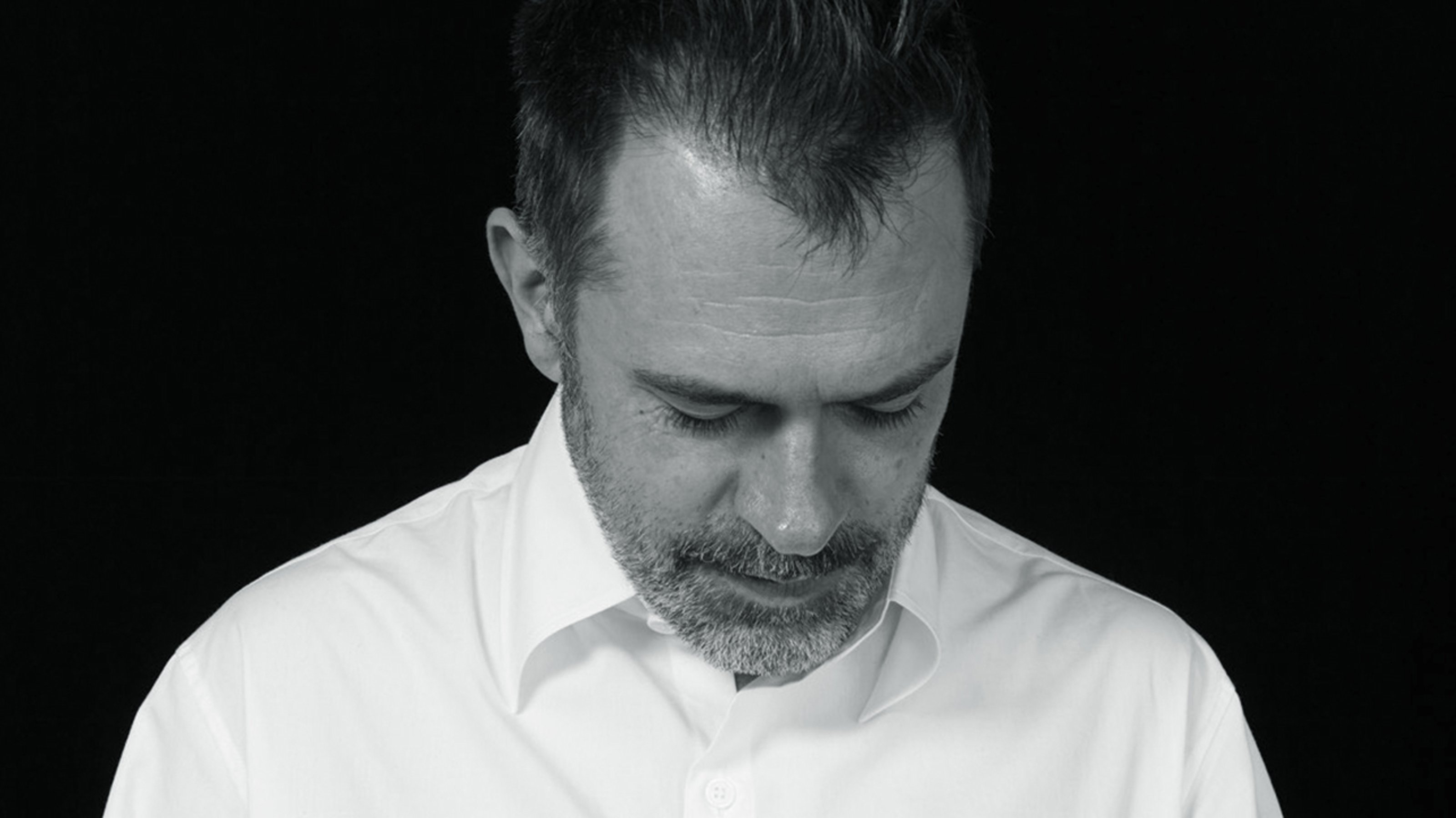 Close-up, black and white photo of Raimundas Malasuaskas, the curator of the now cancelled Russian Pavilion at the 59th Venice Biennale, looking down and smiling