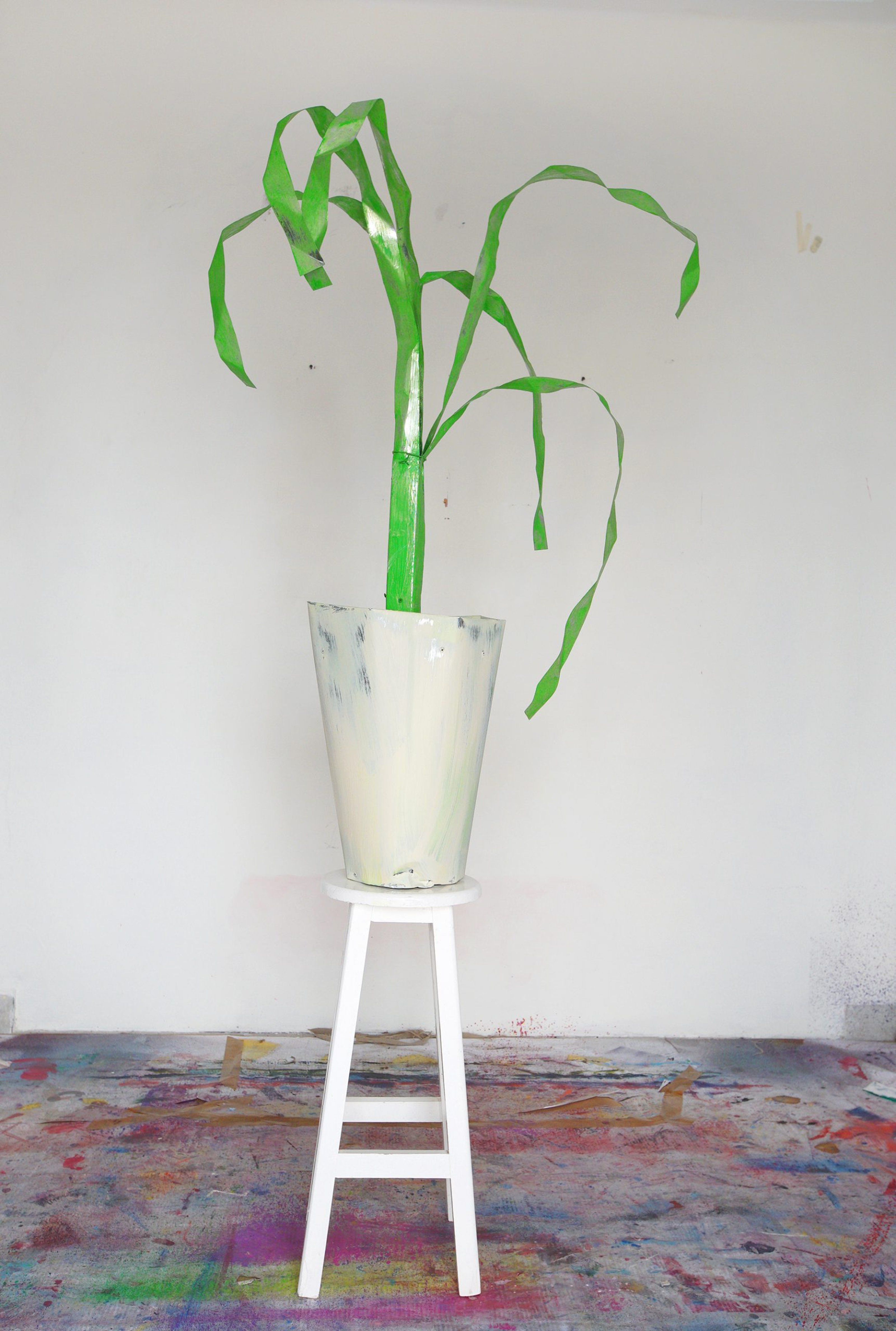 Sculpture of a potted plant, made from sheet metal, wood, oil paint. Placed in the artist's studio on a stool
