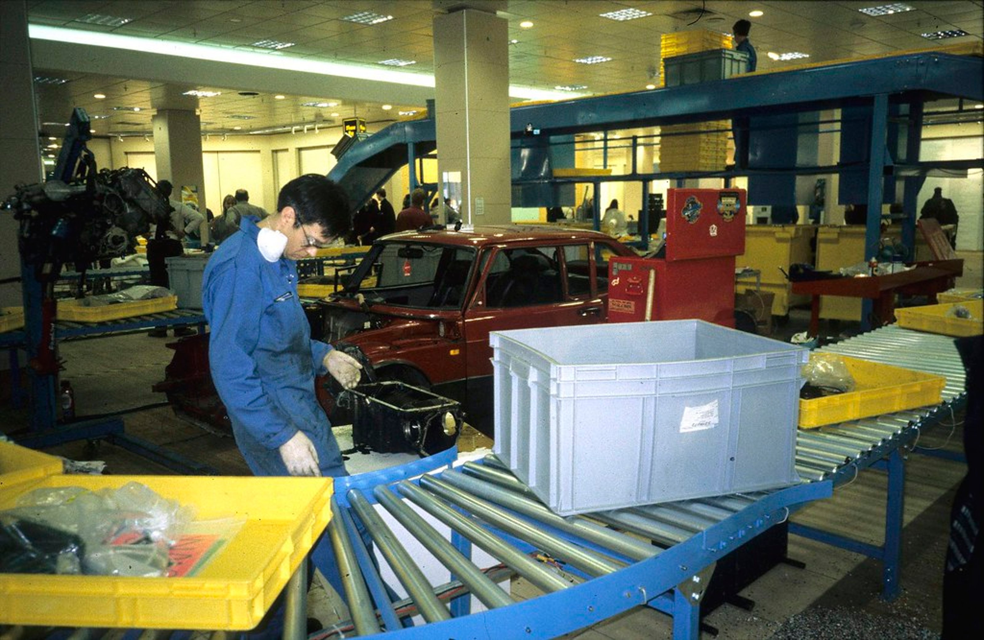 A man in blue industrial suit working behind a conveyor belt. Boxes and shelves items are transporting by the conveyor belt.