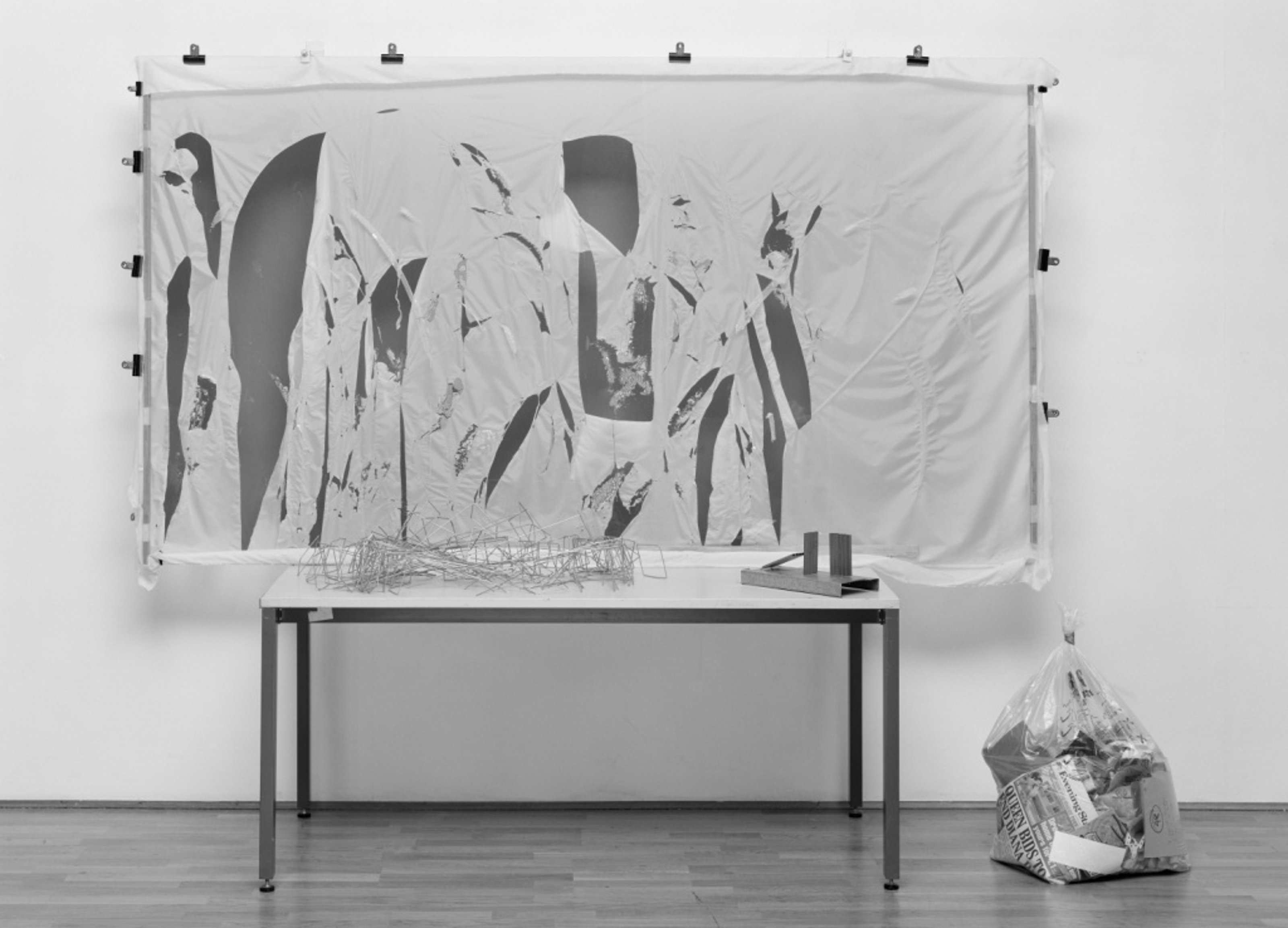 A disintegrated linen canvas is placed on an easel and bag of fabric is to the right on the floor.