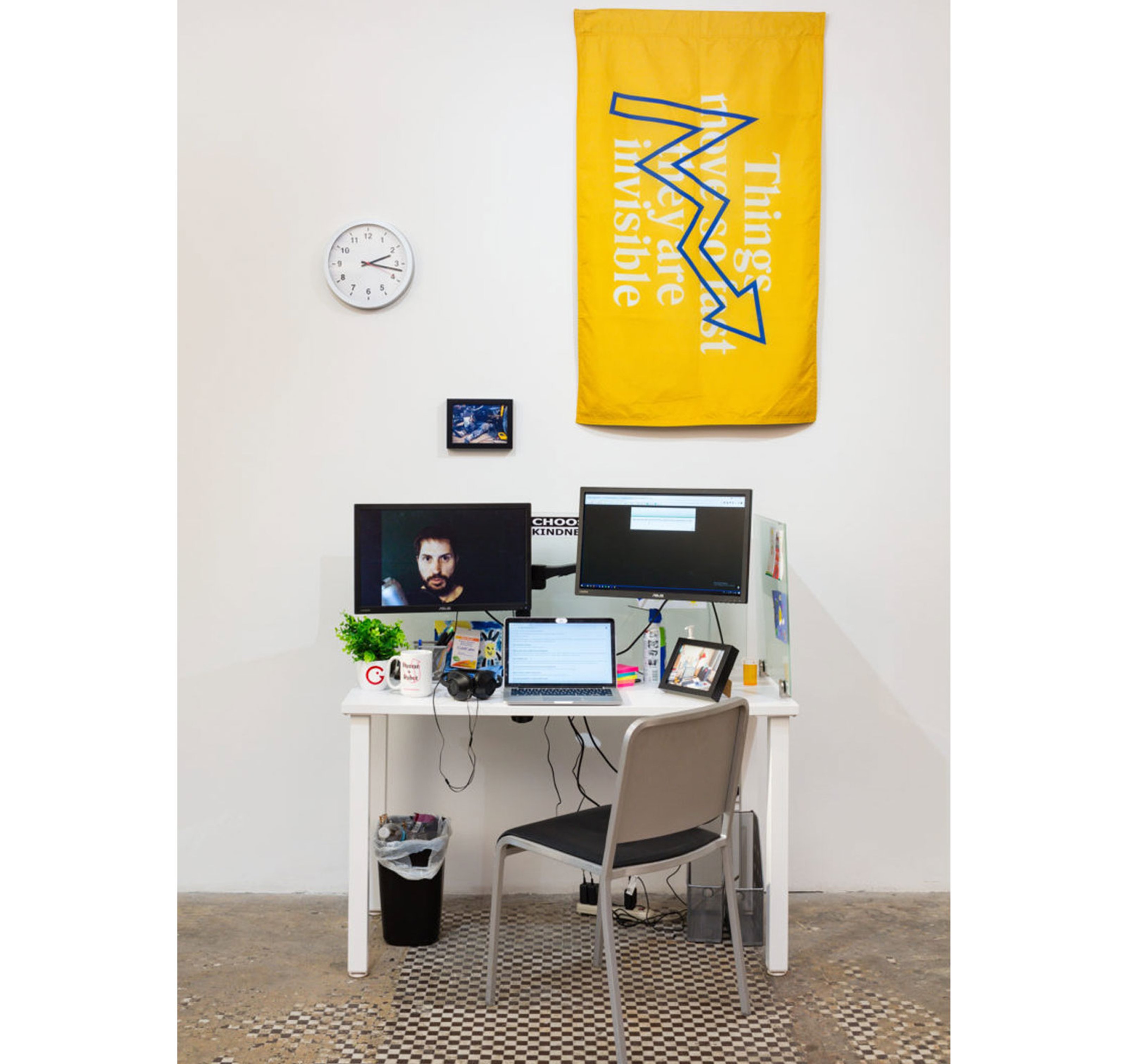 An artwork showing a working table with a laptop and stationary and tapestry on the wall.