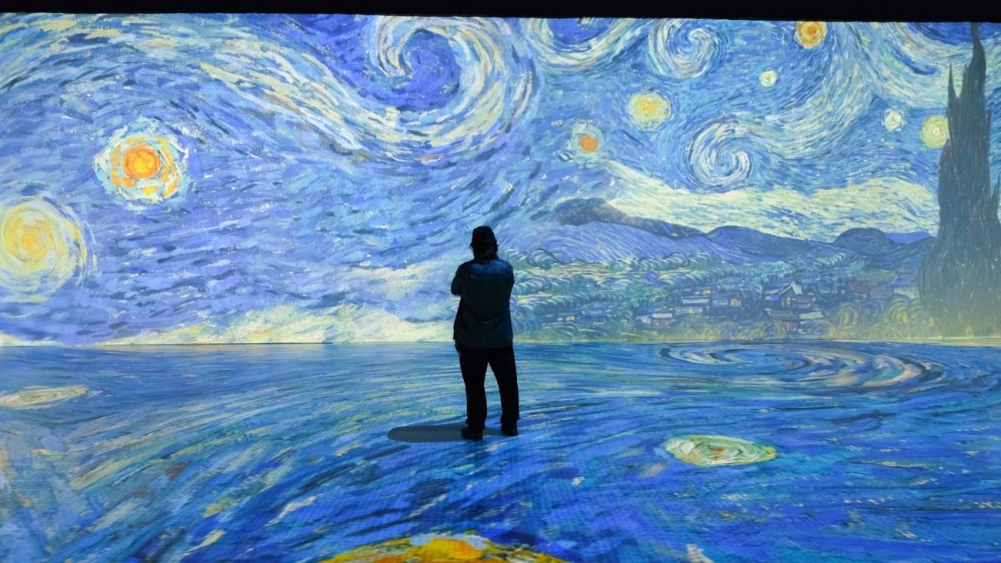 A visitor views Van Gogh's Starry Night projected on a wall and the floor in the immersive Van Gogh Exhibition, Beyond Van Gogh