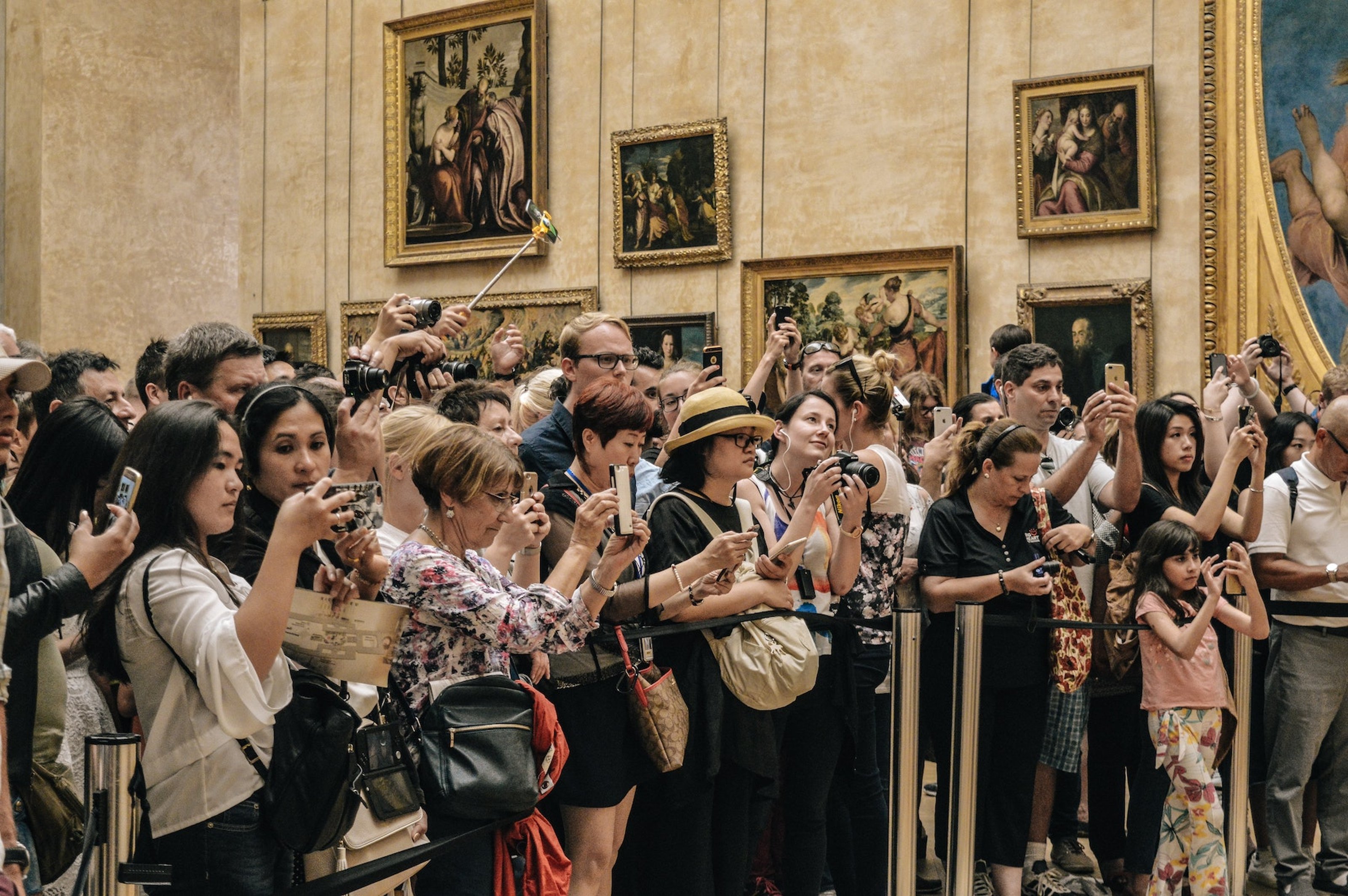 Visitors with phones and selfie sticks in their hands, crowed in a gallery in the Louvre.