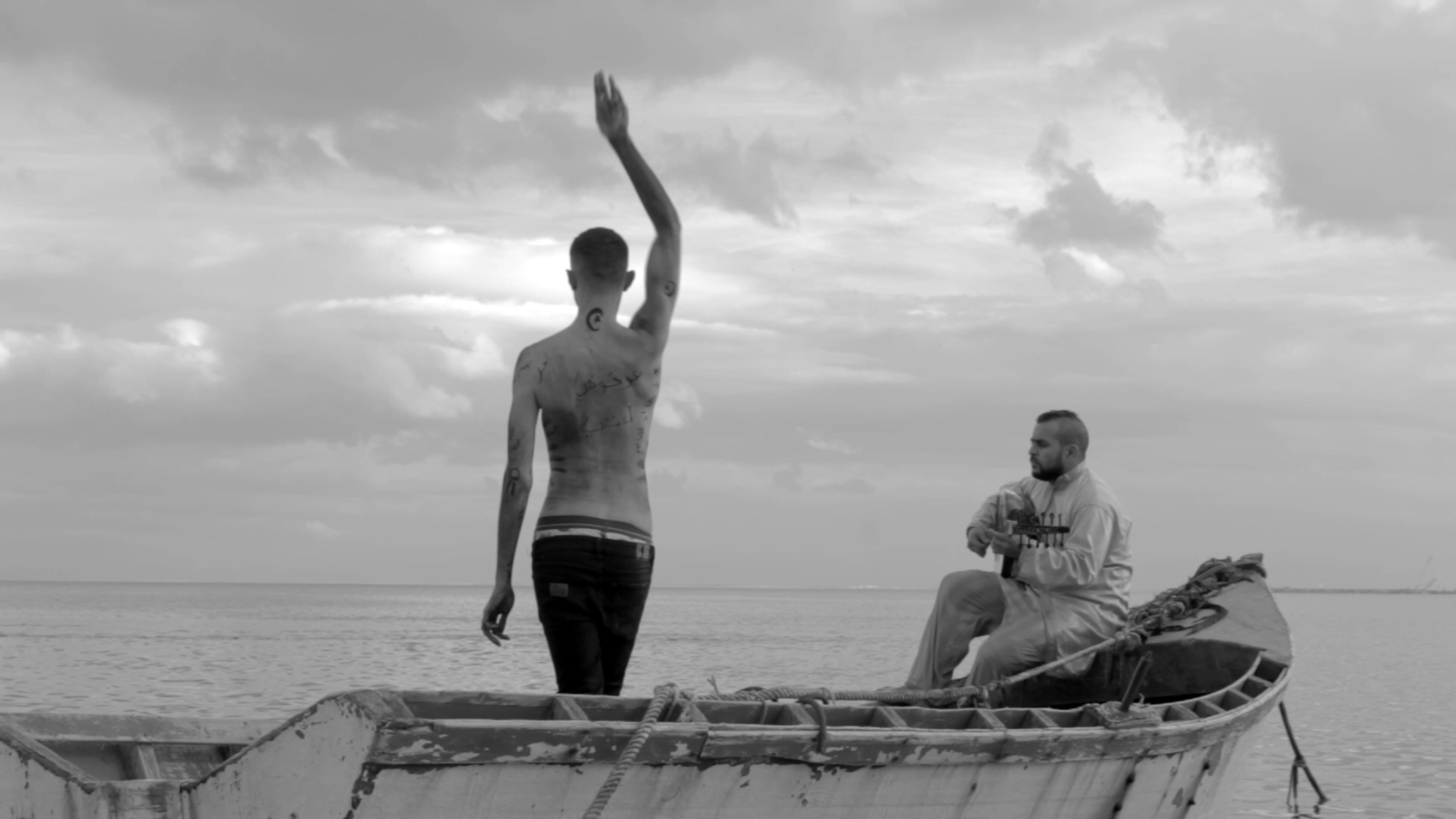Dos hombres en un barco en el mar. Uno está tocando el laúd, el otro está de pie de espaldas y con la mano levantada.