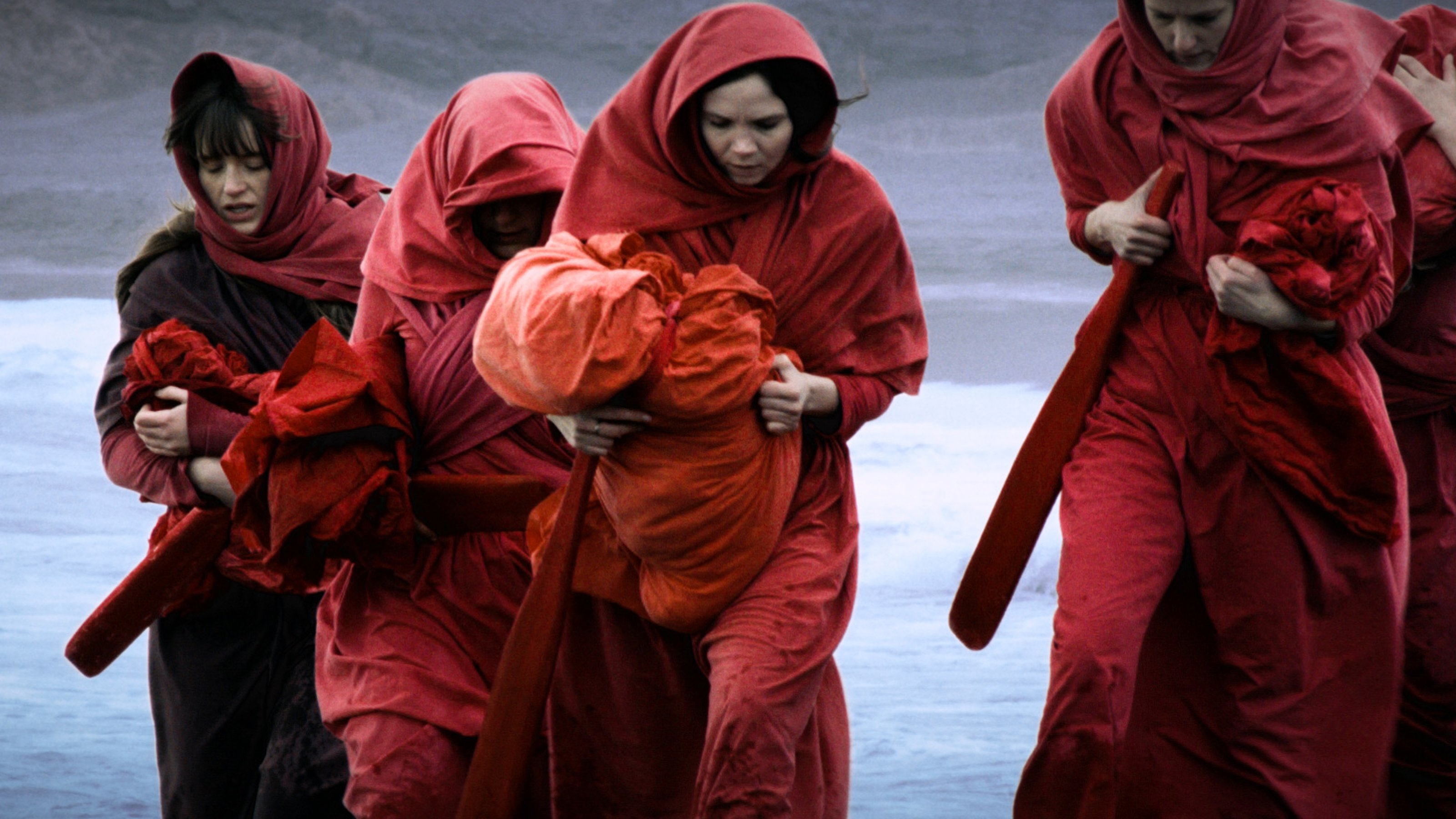 Un grupo de mujeres sosteniendo paños caminando por la orilla contra el viento.