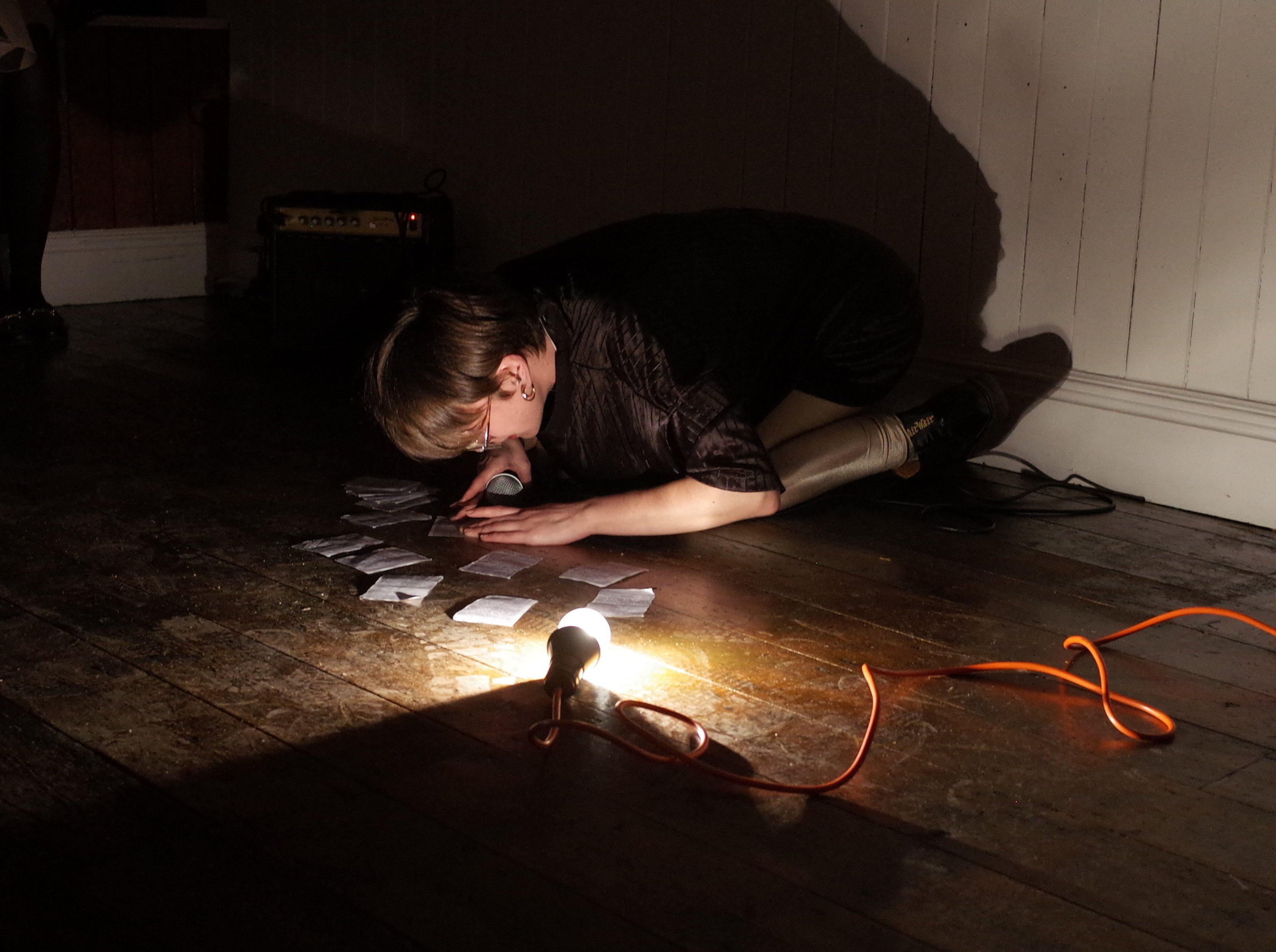 Performance, Roy Claire Potter kneeling down to pieces of paper, reading with a dim light.