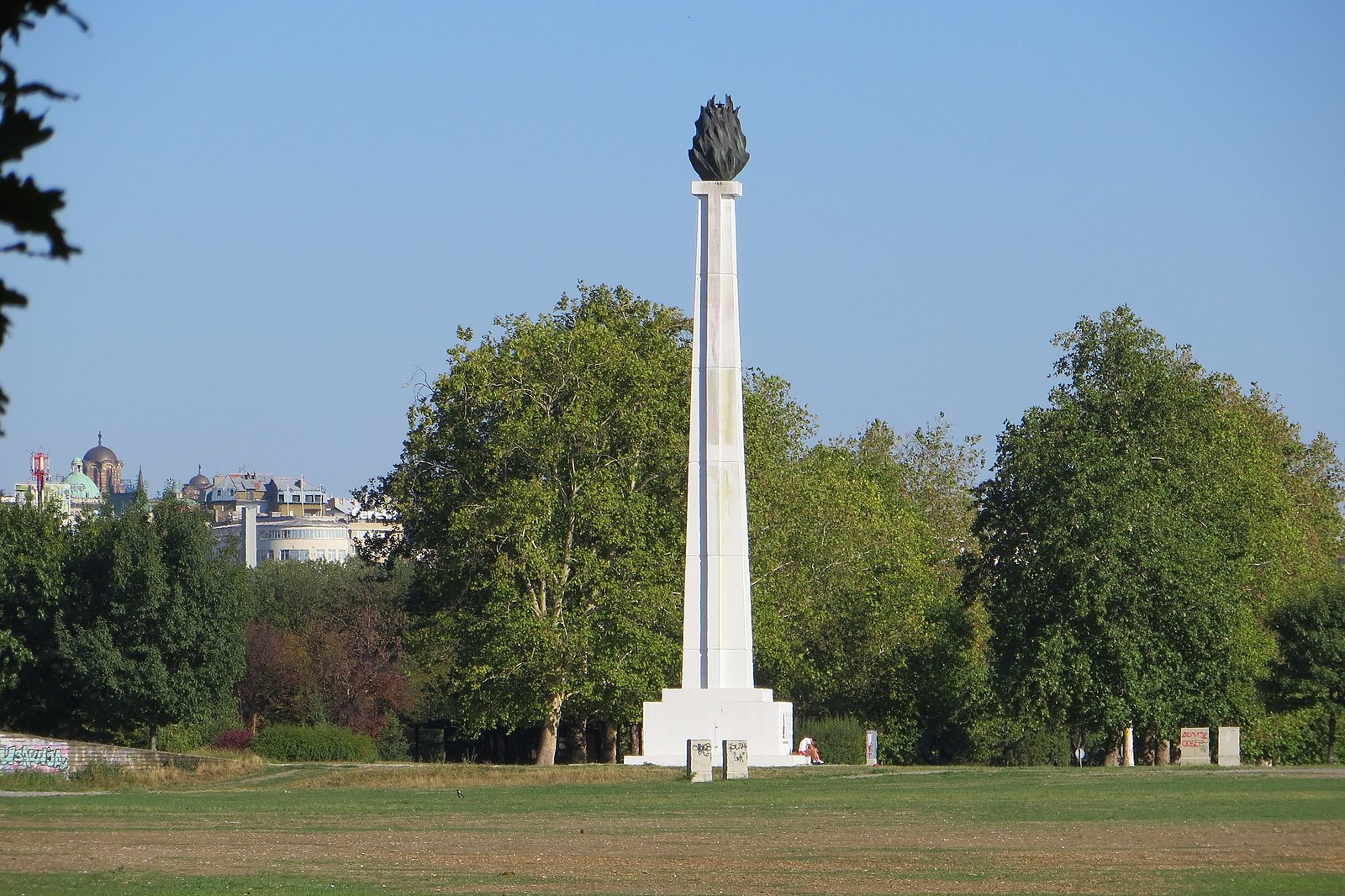 Friendship Park in New Belgrade, a monument stands in an open field with trees behind it